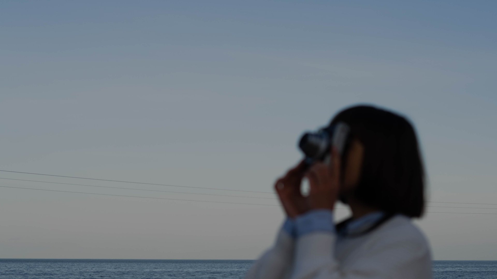 Silhouette of a Woman Taking a Photo of the Ocean Under the Moonlight at Dusk.