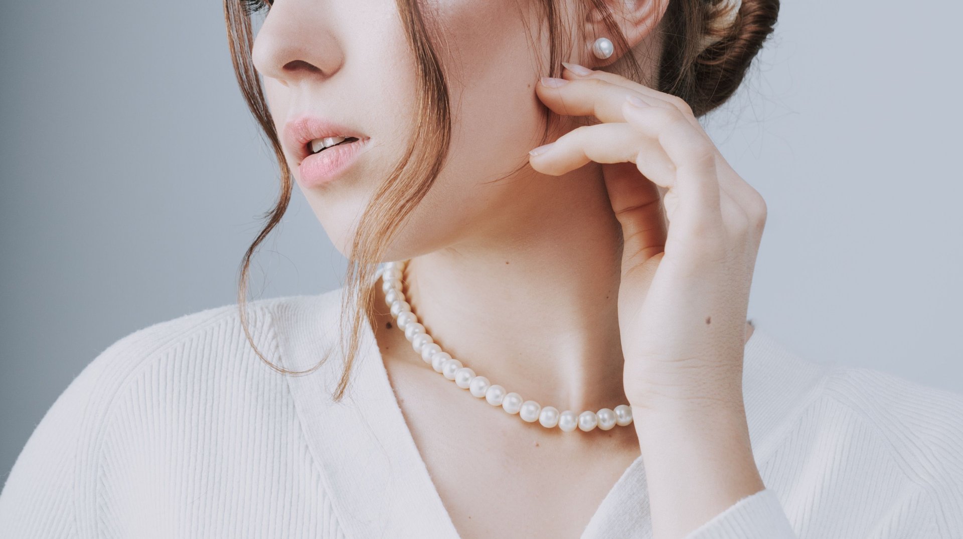 a Refined Portrait of a Brunette Woman with a Pearl Necklace and White Cardigan, Exuding Elegance and Simplicity.