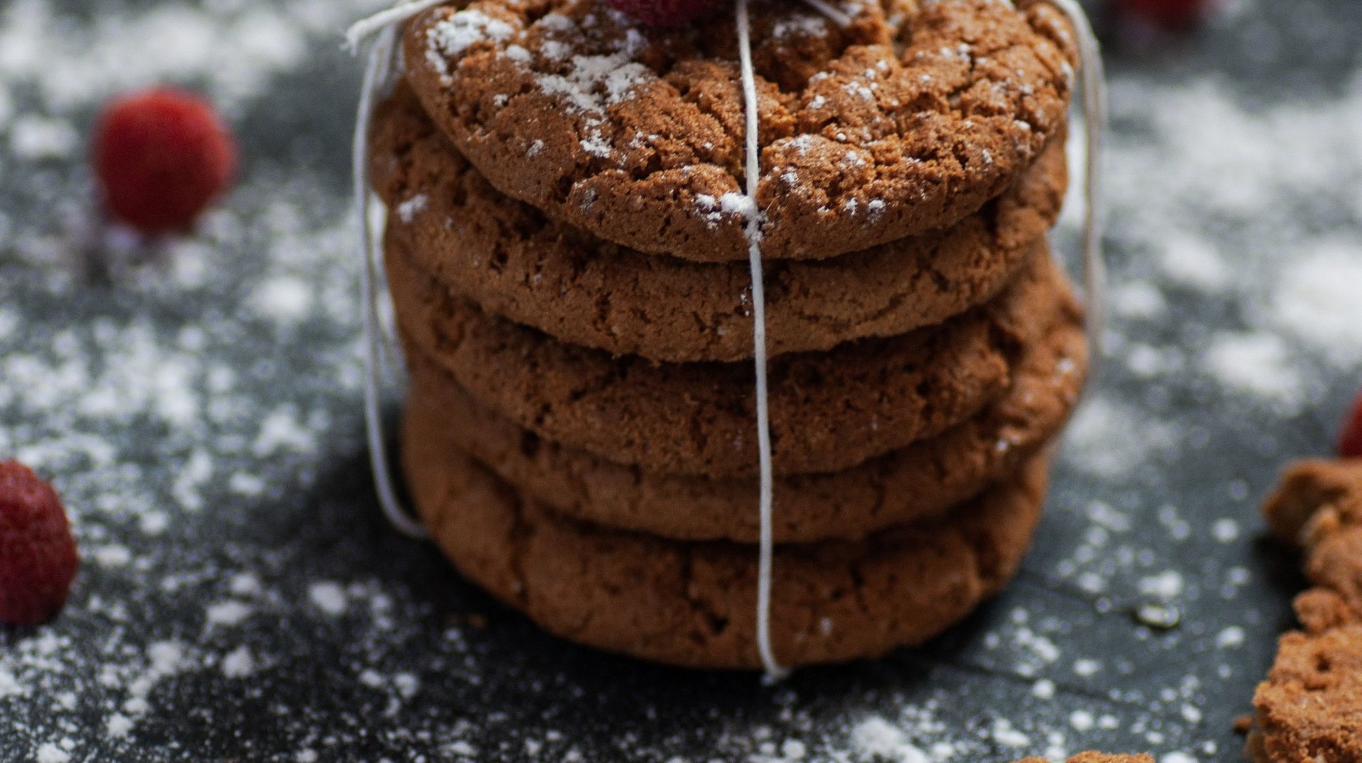 Stack of Chocolate Cookies Topped with Raspberries and Dusted with Powdered Sugar on a Dark Background.