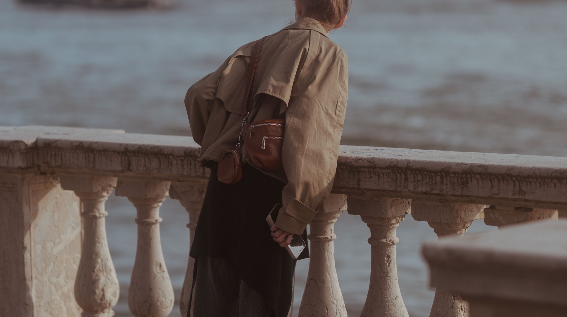 a Woman Leans on a Balcony in Venice, Italy, Overlooking a Serene Waterfront Under a Cloudy Sky.