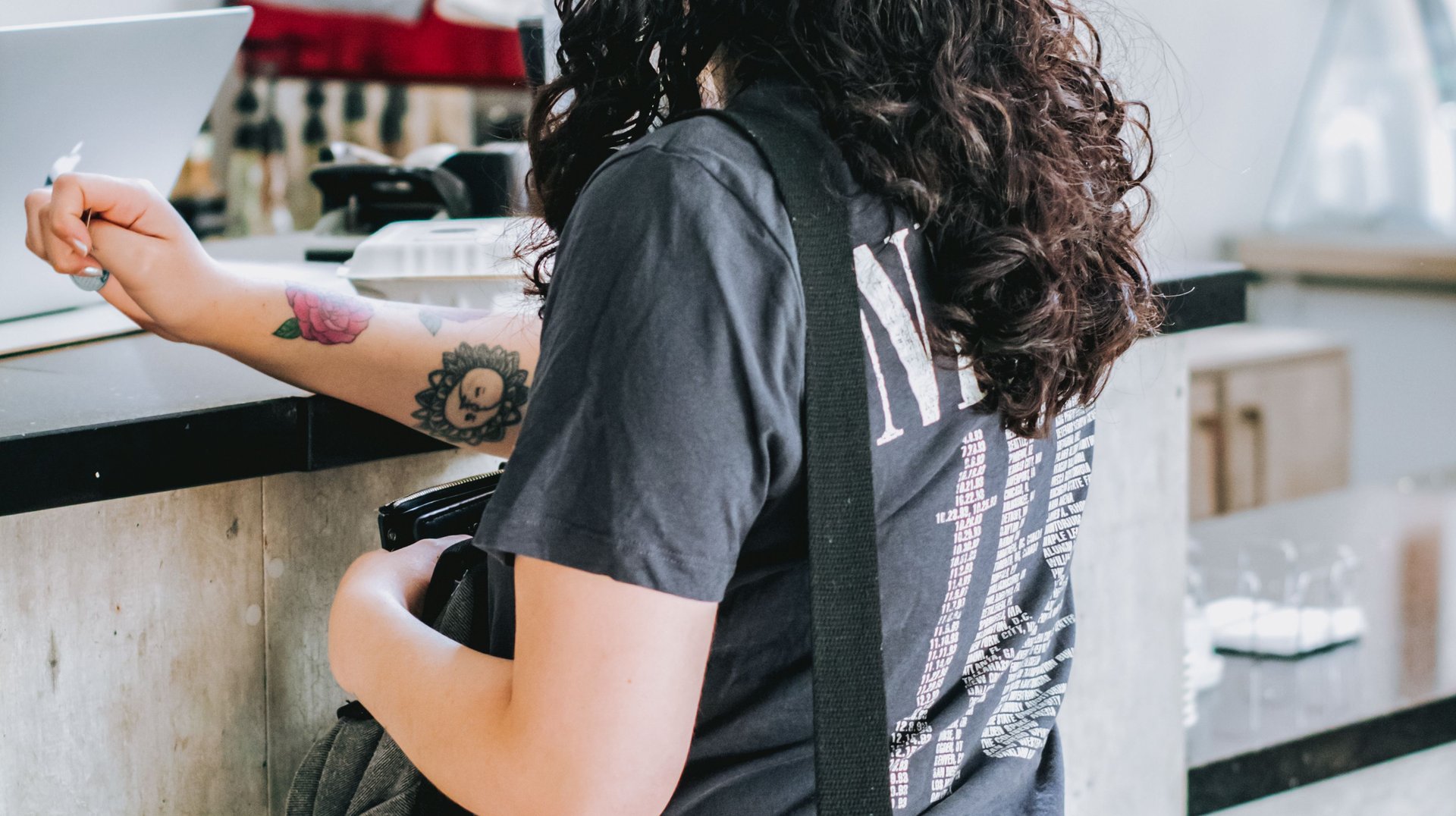 Young Woman with Curly Hair Orders at a Coffee Shop Counter, Exuding Casual Coffee Shop Vibes.