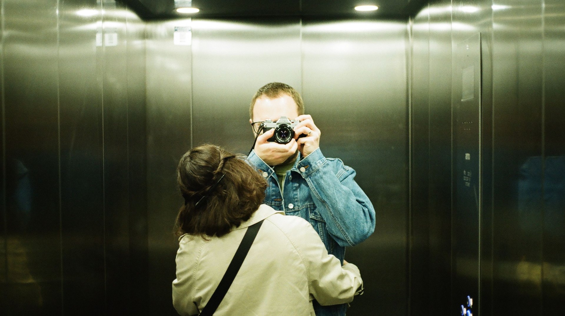 a Couple Captures a Nostalgic Mirror Selfie in an Elevator Using a Vintage Film Camera.
