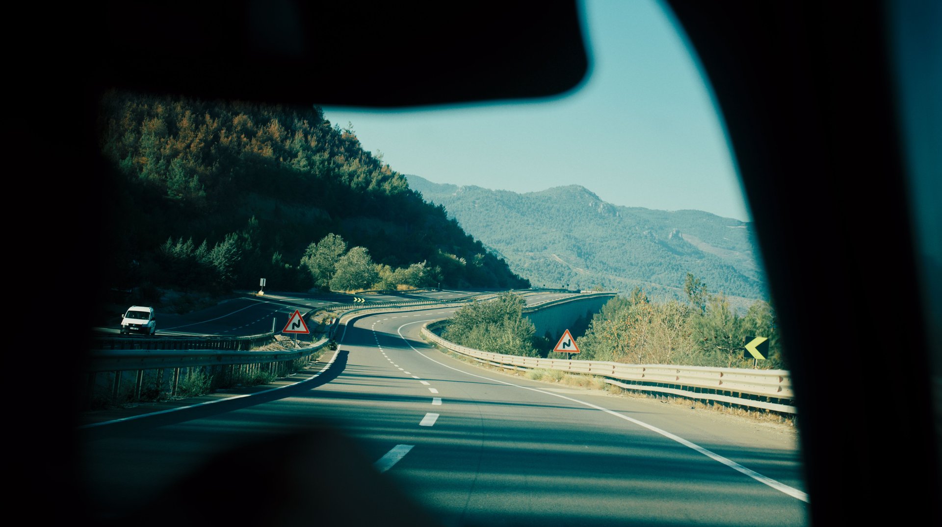 a Scenic View of a Winding Highway Passing Through Lush Mountains, Captured From Inside a Vehicle.