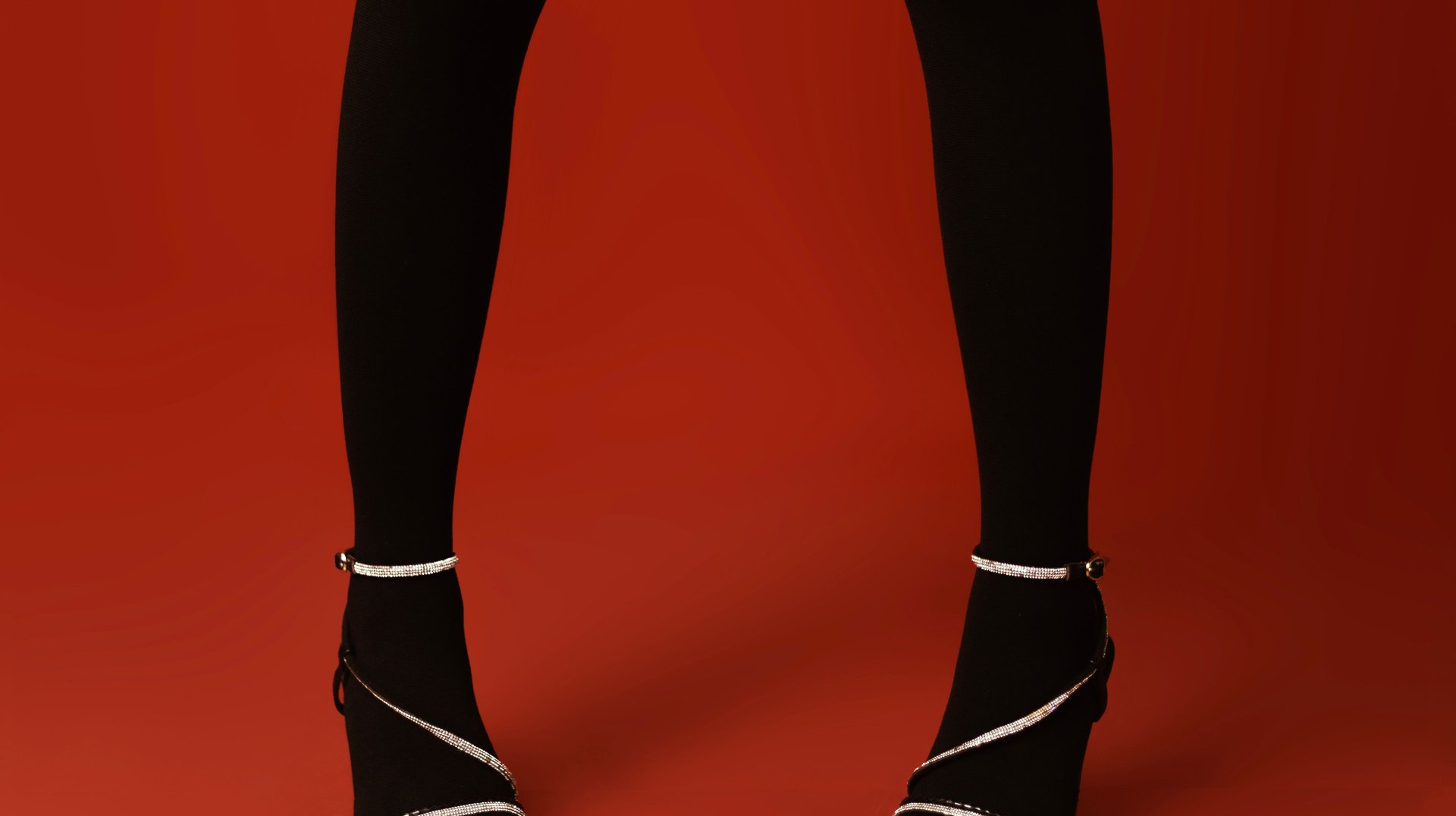 Fashionable Black Tights and Heels Against Bold Red Backdrop, Highlighting Style.