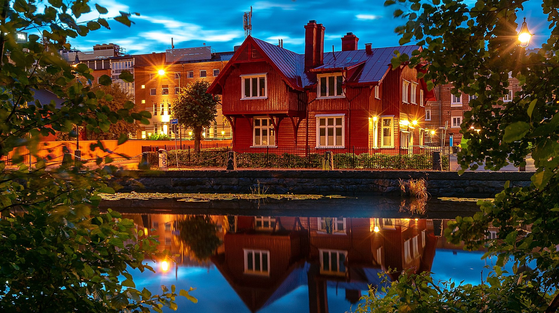 a Picturesque View of a Red House Reflecting in the Water, Framed by Trees in Göteborg, Sweden During Twilight.