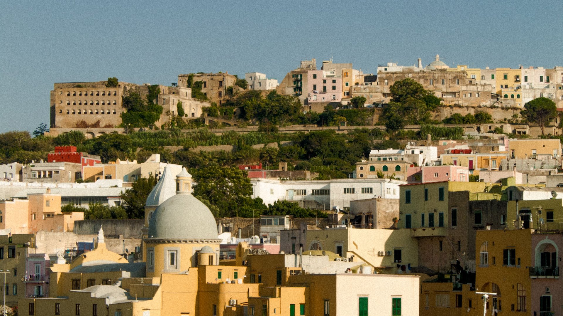 Colorful Buildings Line the Idyllic Harbor of Procida Island, Campania, Italy, Under a Clear Blue Sky.