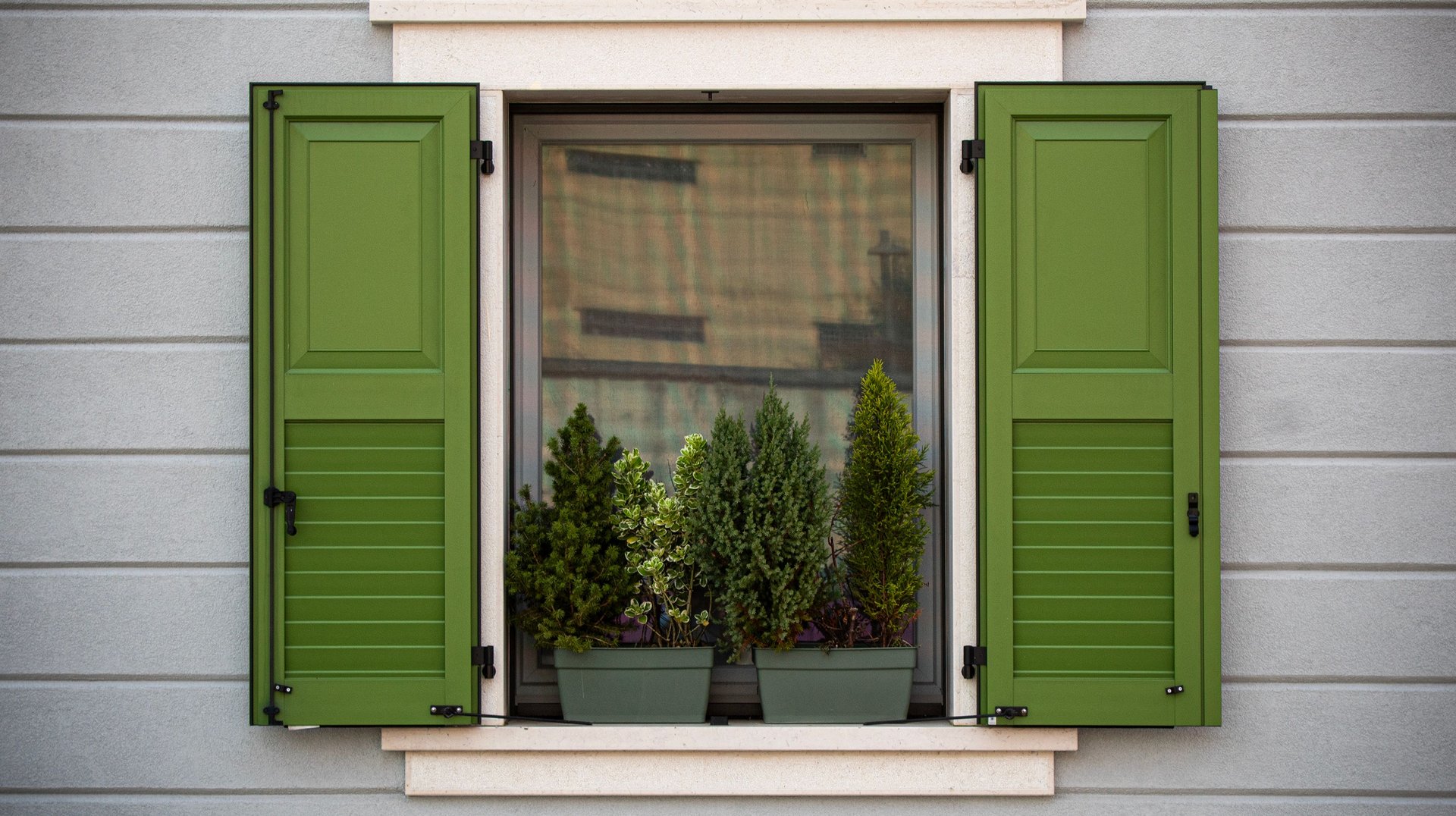 a Picturesque Window in Palmanova, Italy, Featuring Green Shutters and Potted Evergreen Plants.