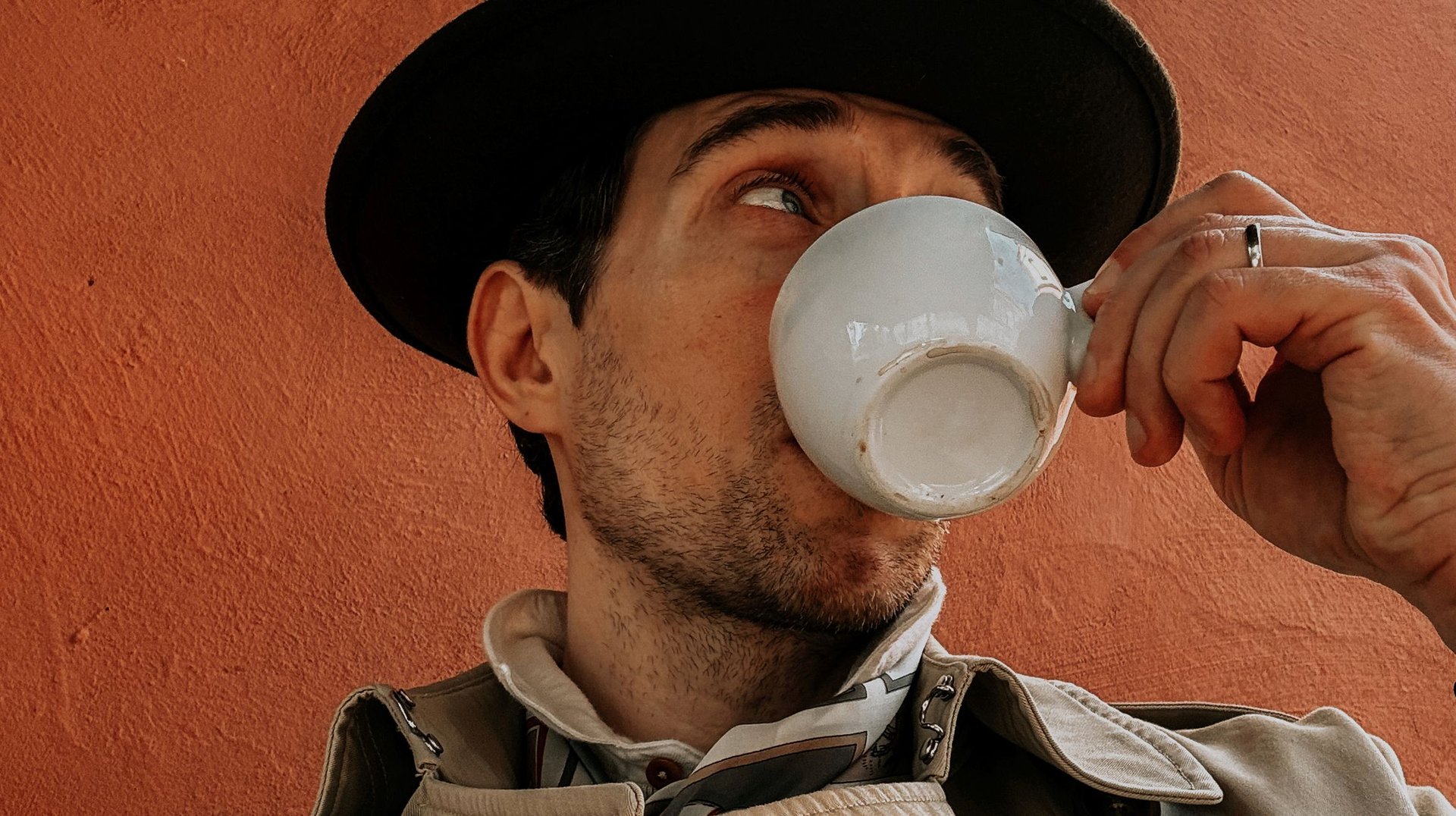 a Fashionable Man Enjoys Coffee Against a Textured Orange Wall in Lower Silesian Voivodeship.