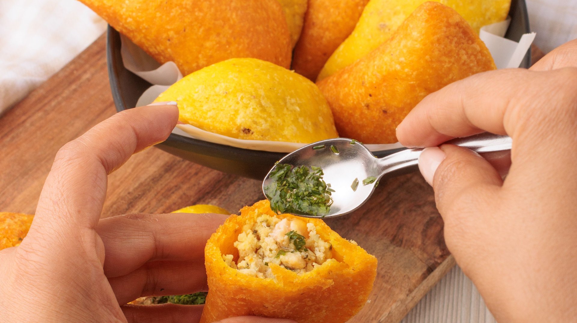 Close-up of Colombian Empanadas Being Garnished with Fresh Herb Sauce, Highlighting Traditional Flavors.
