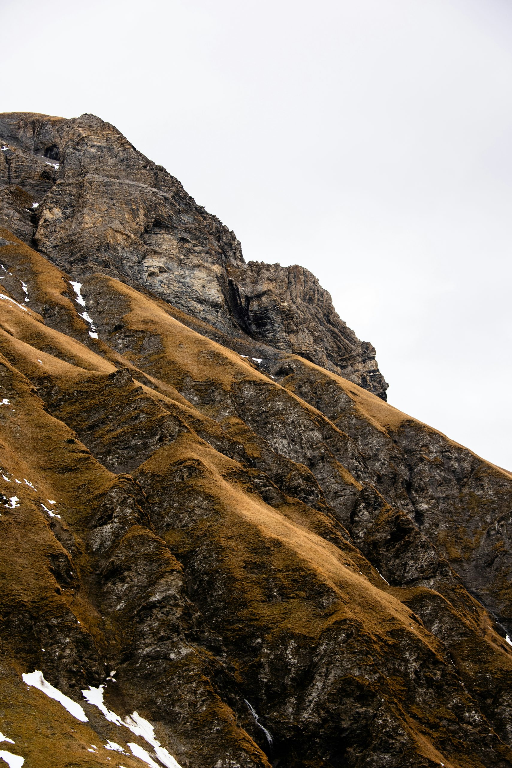 Rocky mountain slope with dry grass and snow
