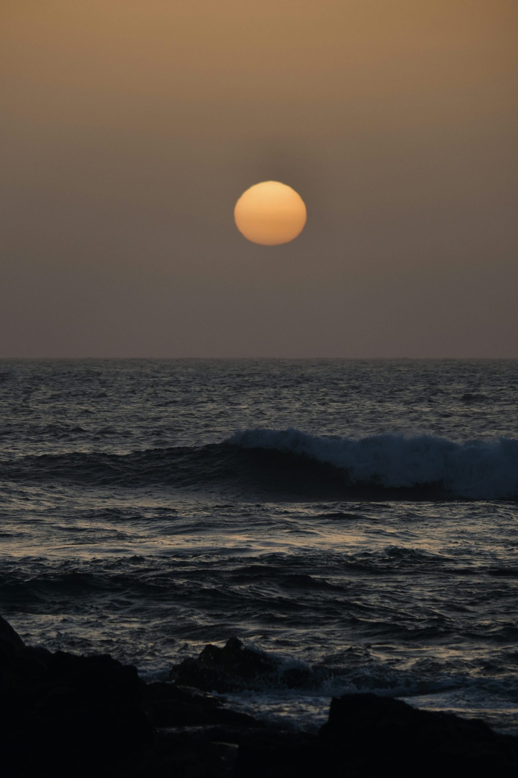 A Large Orange Sun Setting Over A Dark, Choppy Ocean