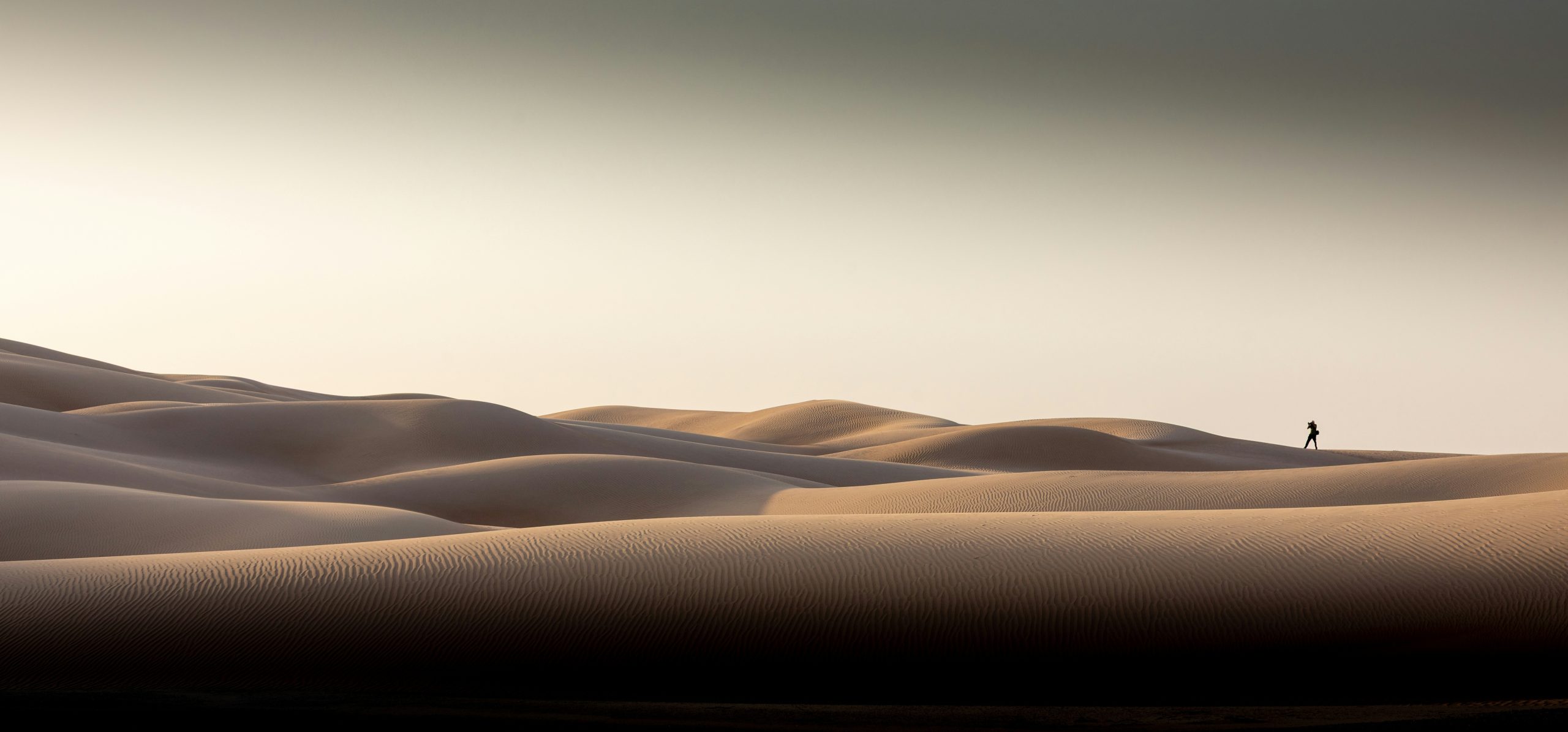 A lone figure stands on rolling sand dunes at sunset