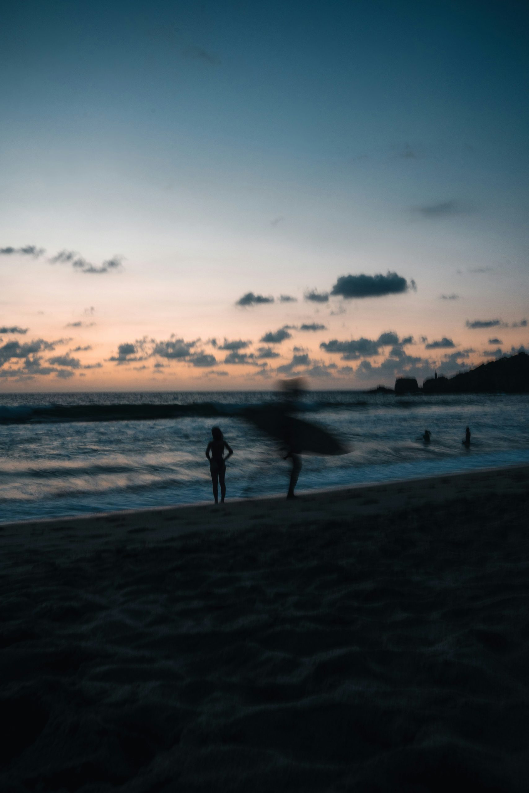 Silhouettes of people on beach at sunset with ocean waves