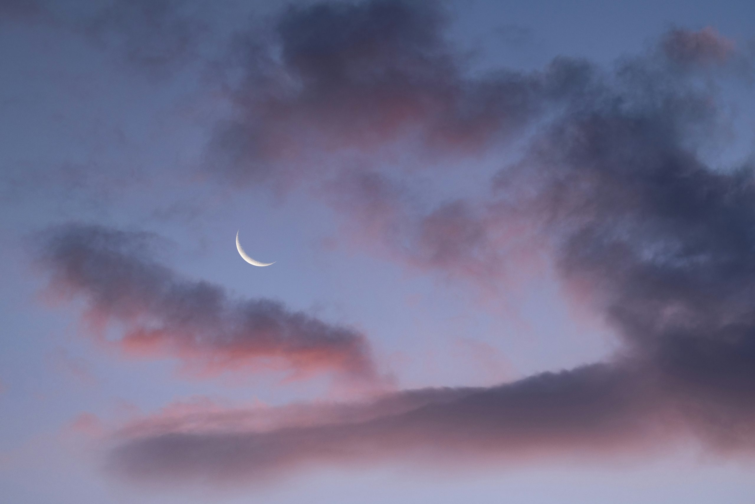 Crescent moon in a serene twilight sky with clouds