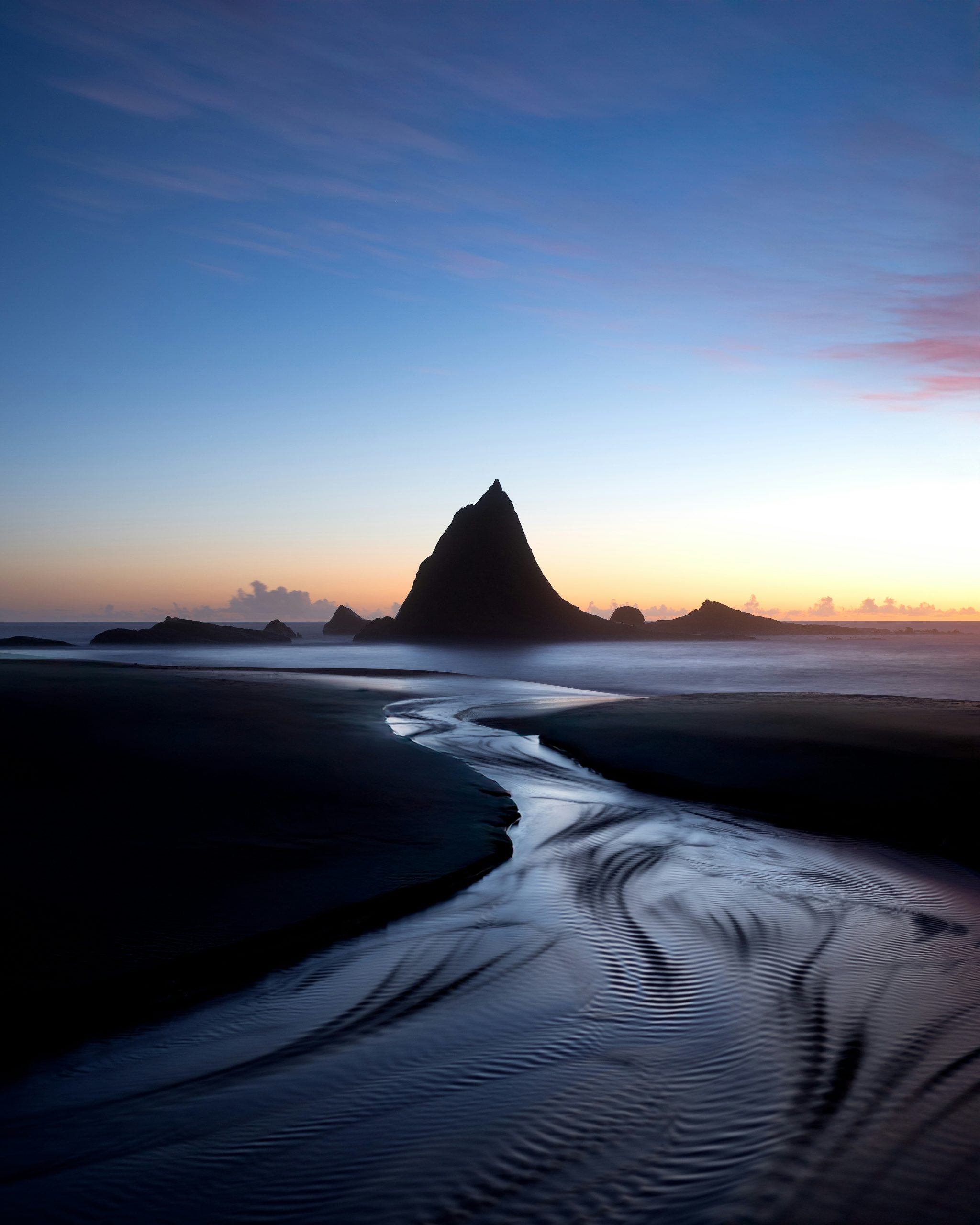 Dark beach stream flowing towards a prominent peak at dusk