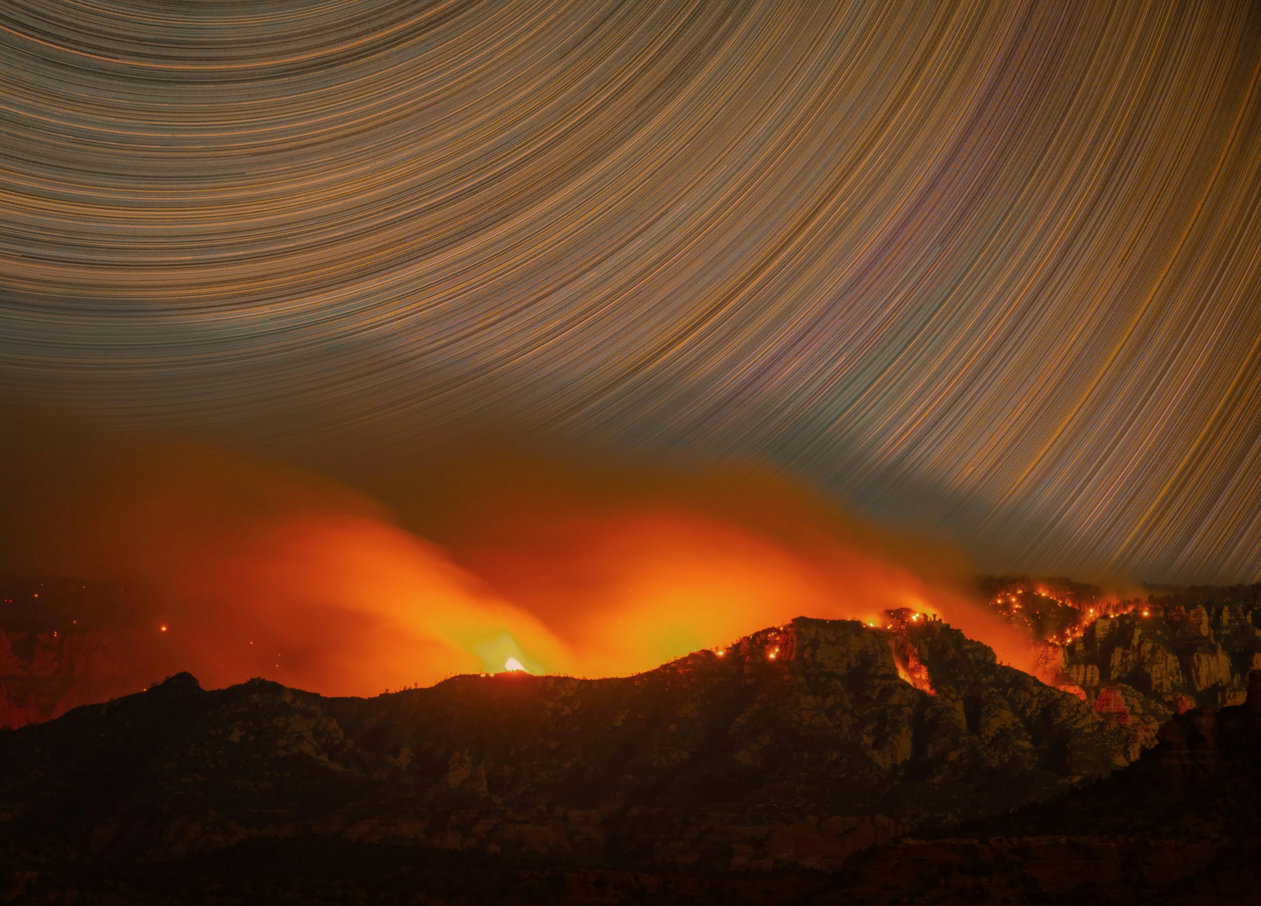 Mountains ablaze with fire under a sky of star trails