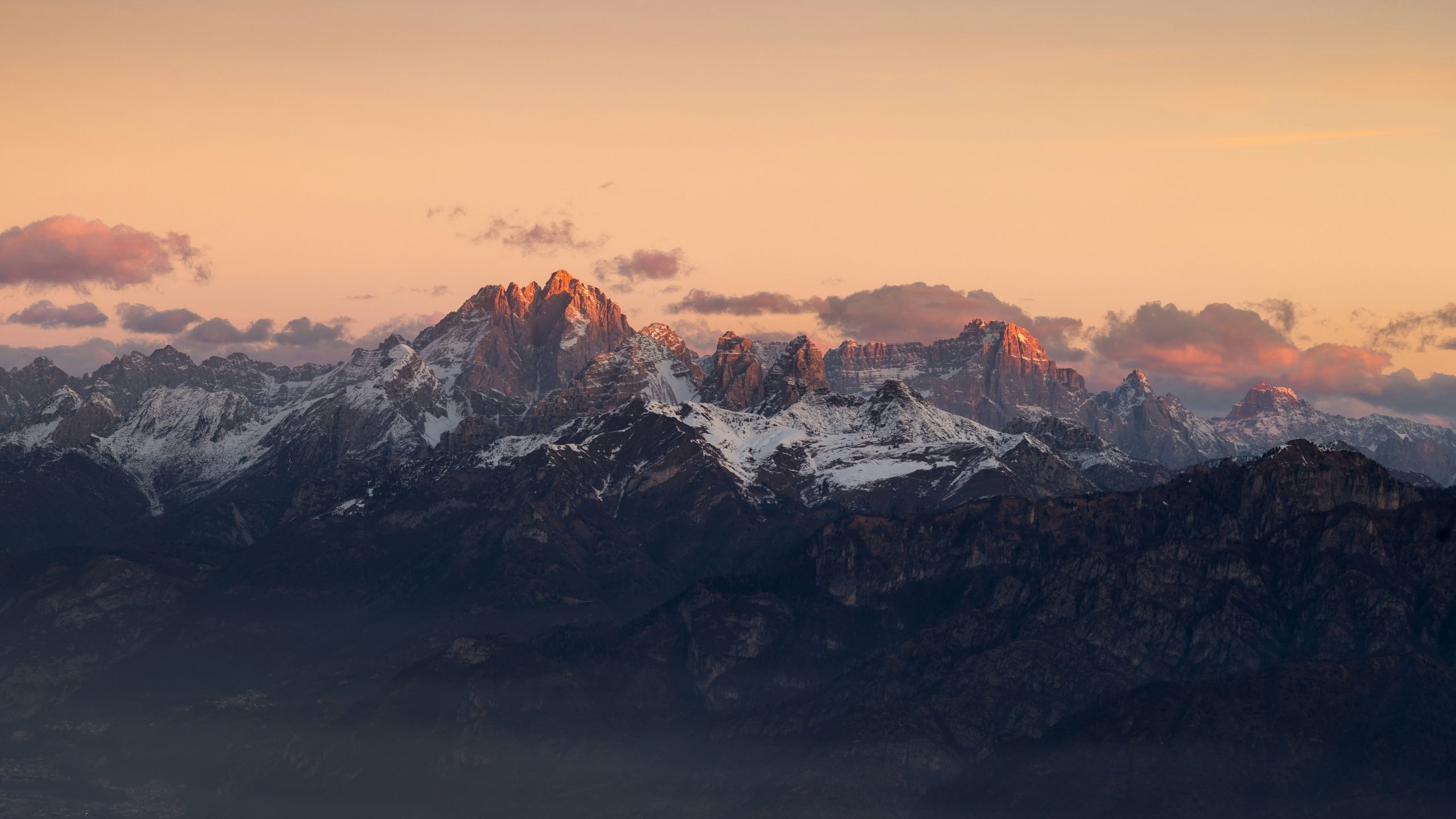 Golden light illuminates rugged snow-capped mountains during sunset