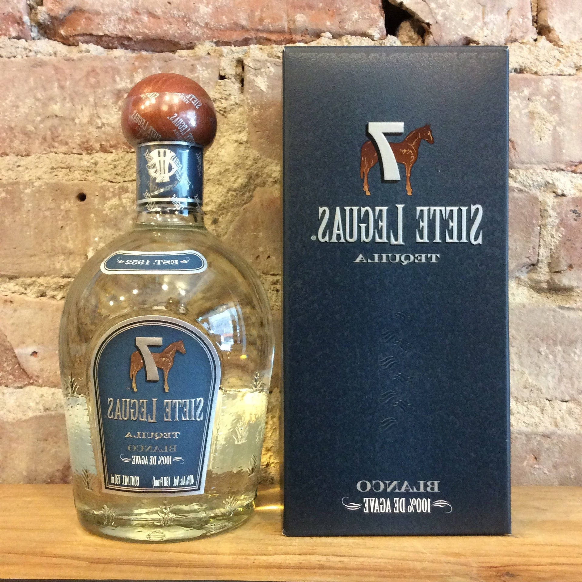 Siete Leguas tequila bottle and box on wood against brick wall.