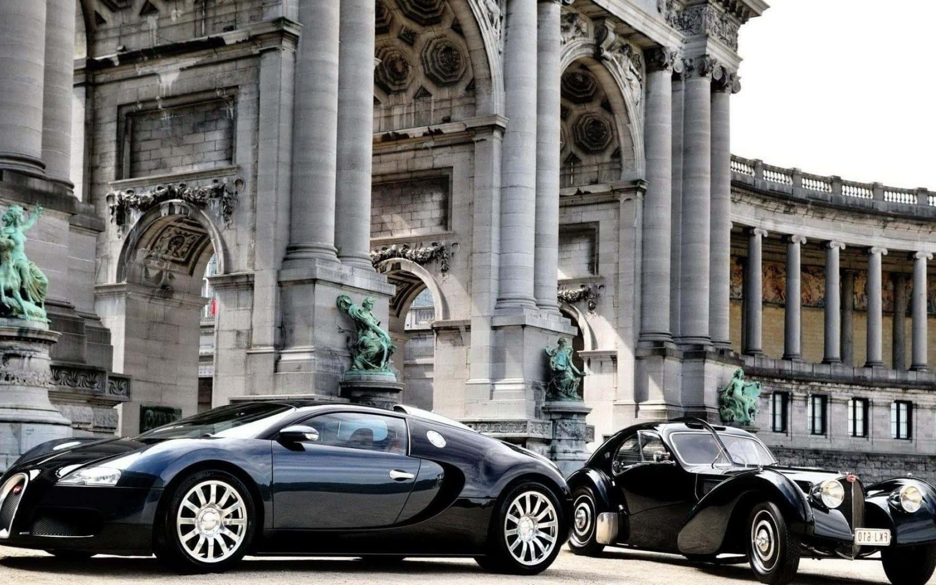 Two Bugatti cars parked in front of a grand stone building with statues.