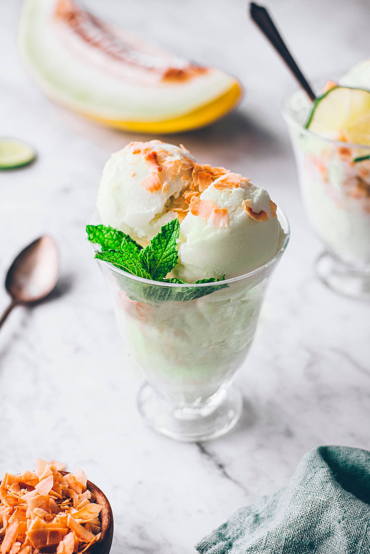 Melon ice cream in glass topped with coconut and mint on marble.