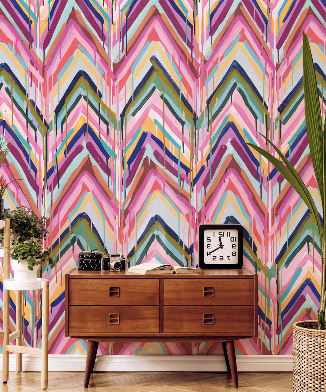 Mid-century dresser with clock camera and book against colorful zigzag wallpaper with dripping paint.