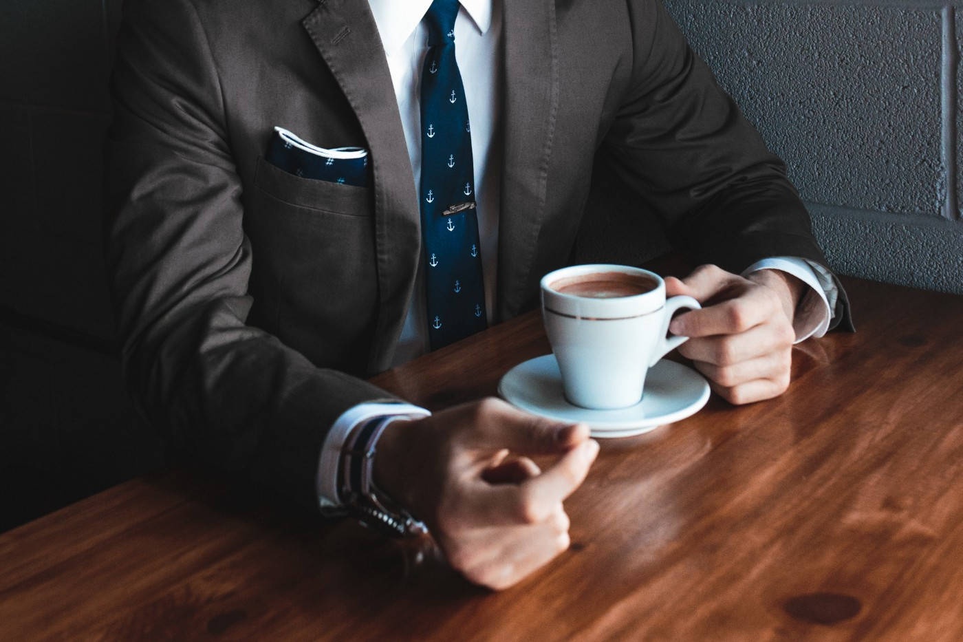 Man in suit holding coffee cup at wooden table in cafe