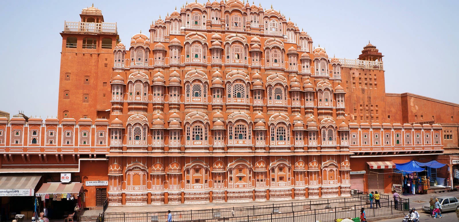 A historic Indian palace with ornate carvings and balconies stands tall above a busy street. – Ultra HD Wallpaper