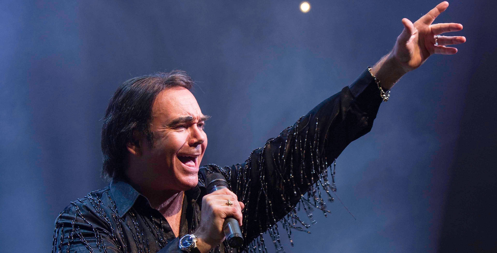 Male singer performing live on stage with raised arm and microphone