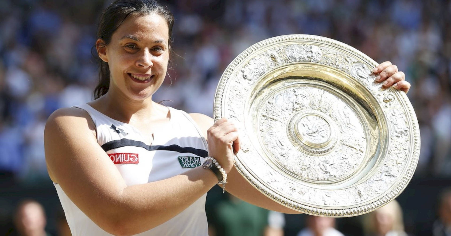 Female tennis player holding silver trophy with crowd in background.