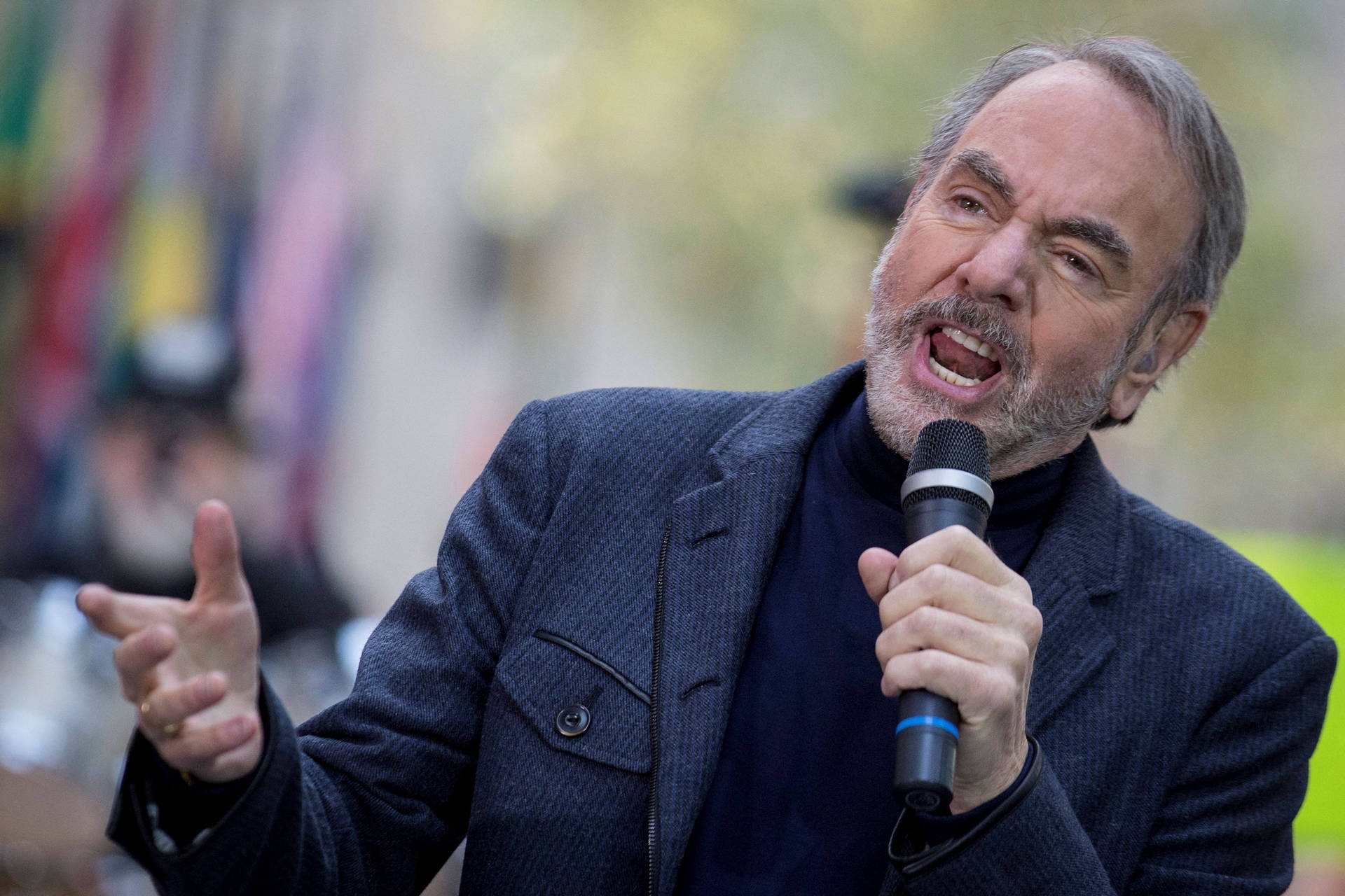 Man speaking into microphone outdoors with expressive gesture.