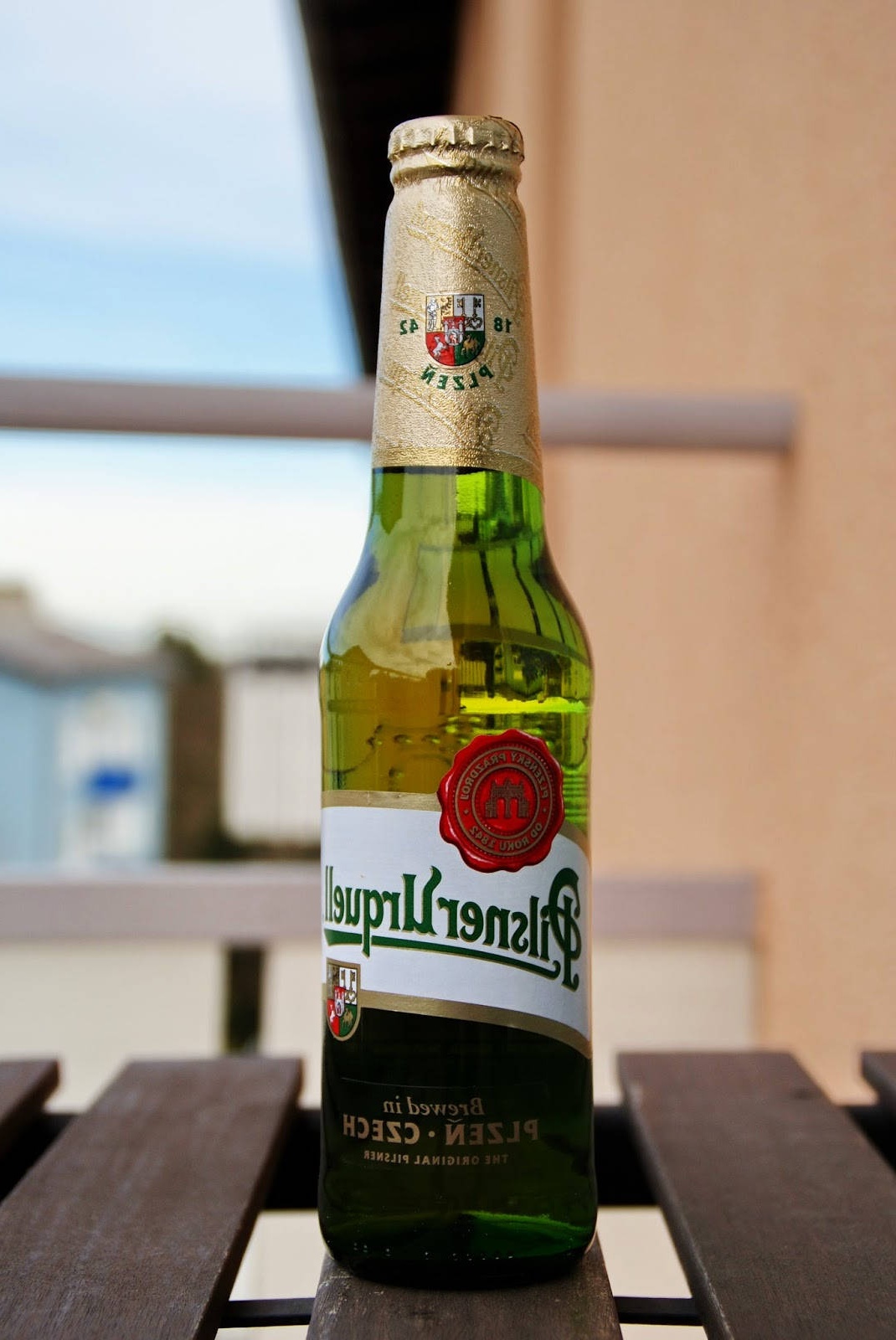 A green Pilsner Urquell beer bottle on a wooden table outdoors.