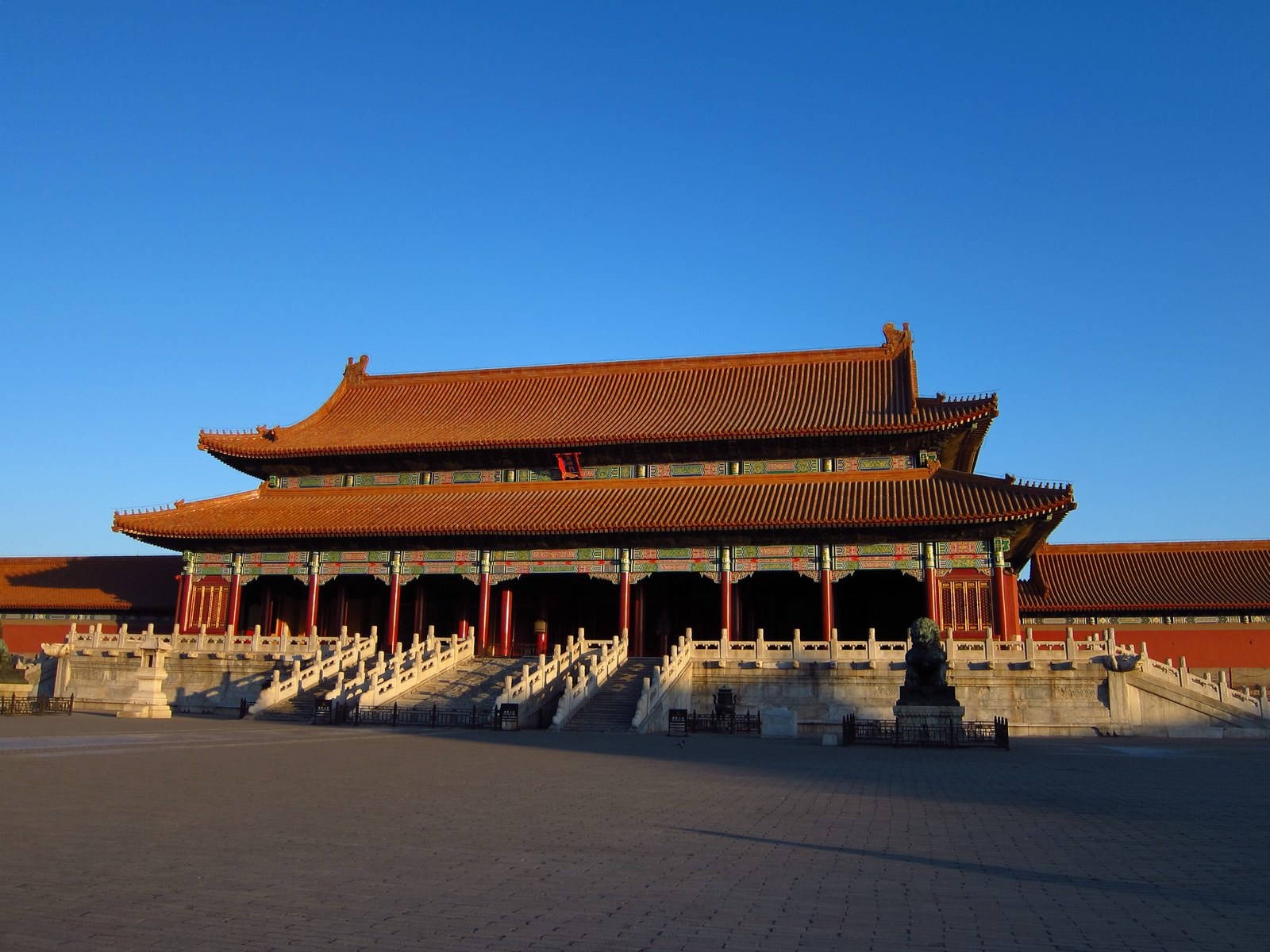 Imposing ancient Chinese palace with orange roofs and red pillars bathed in golden sunset light.