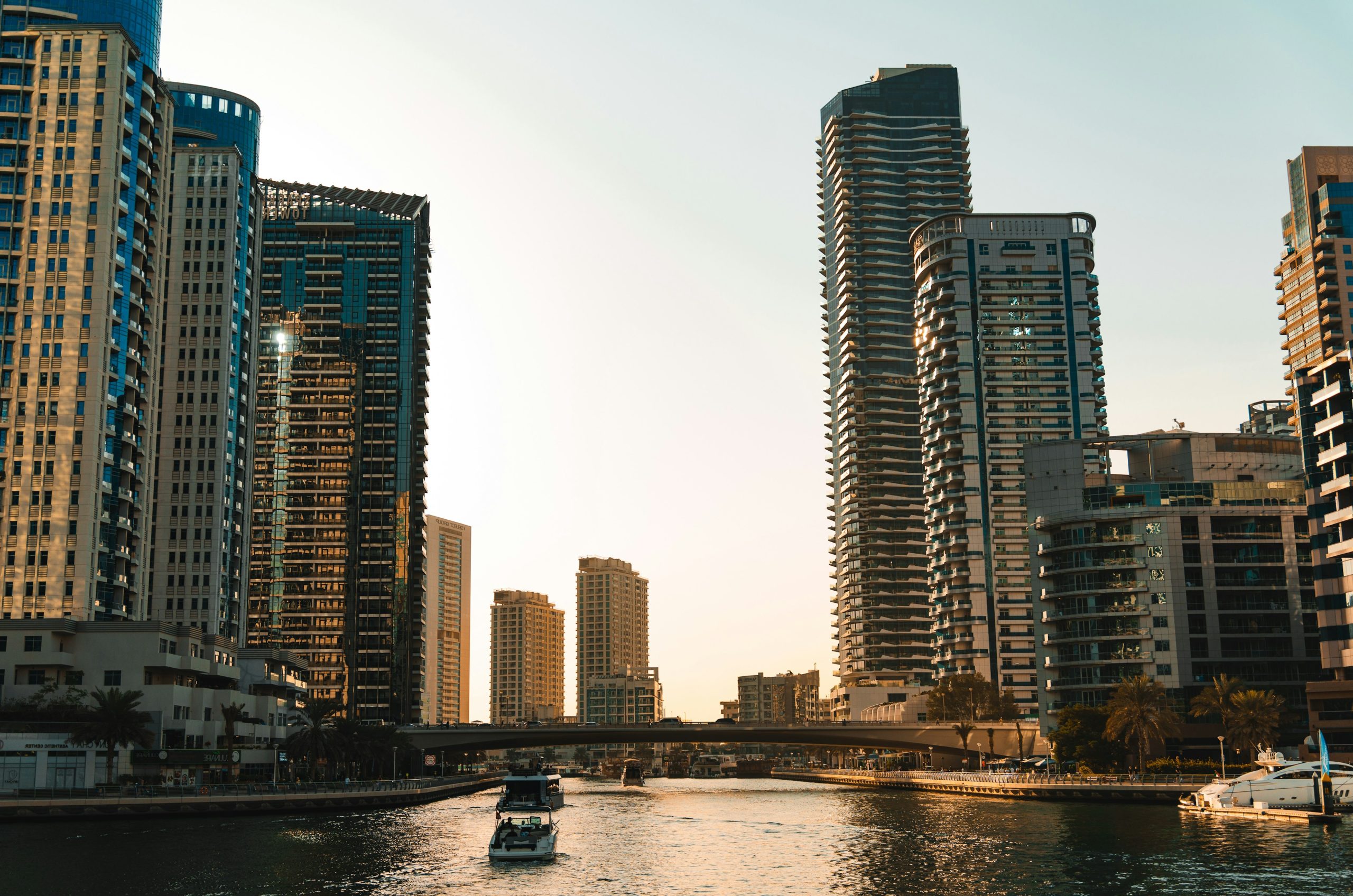 Modern skyscrapers line a calm canal with boats.