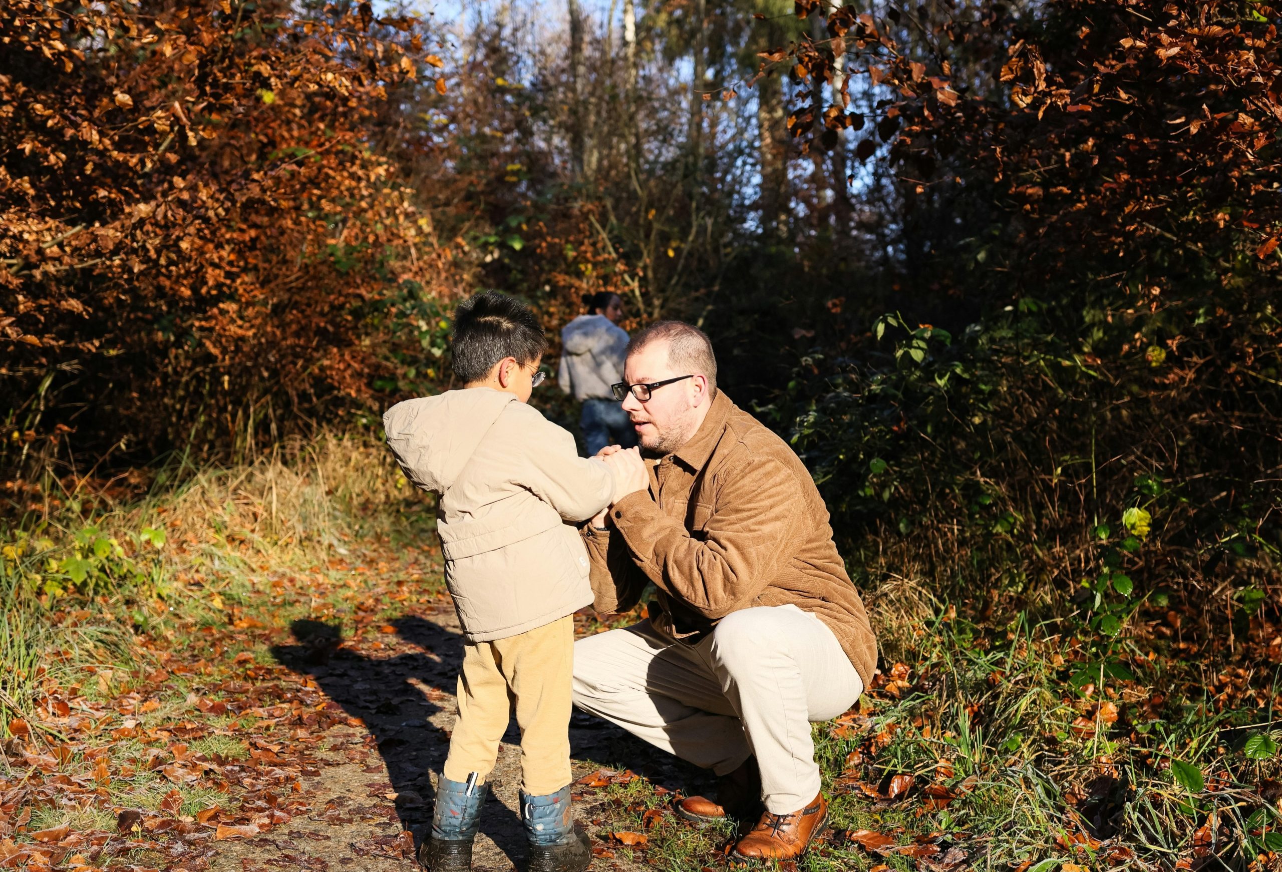 Father and son interact in autumn forest path.