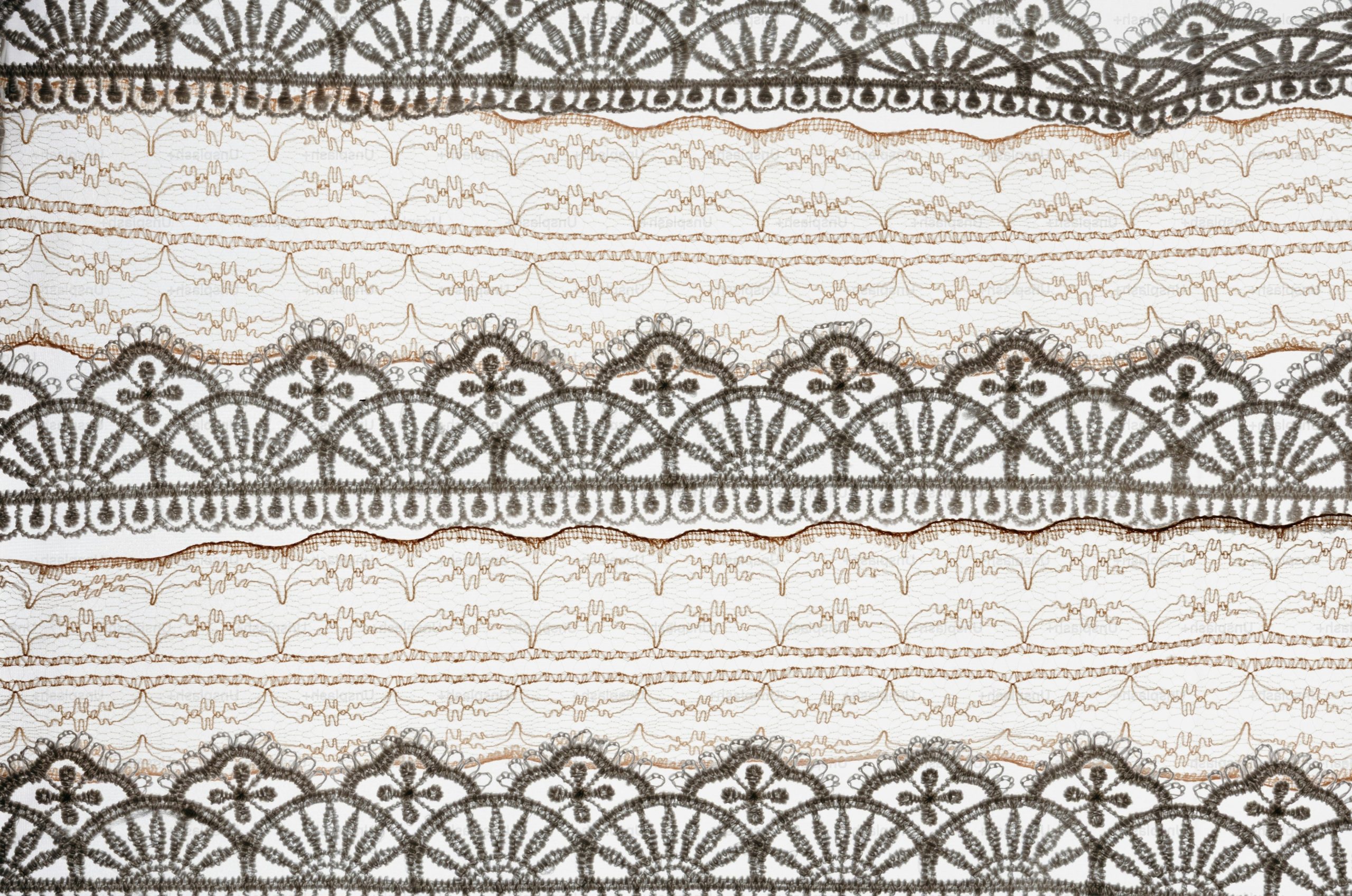 White fabric with intricate grey lace trim patterns.