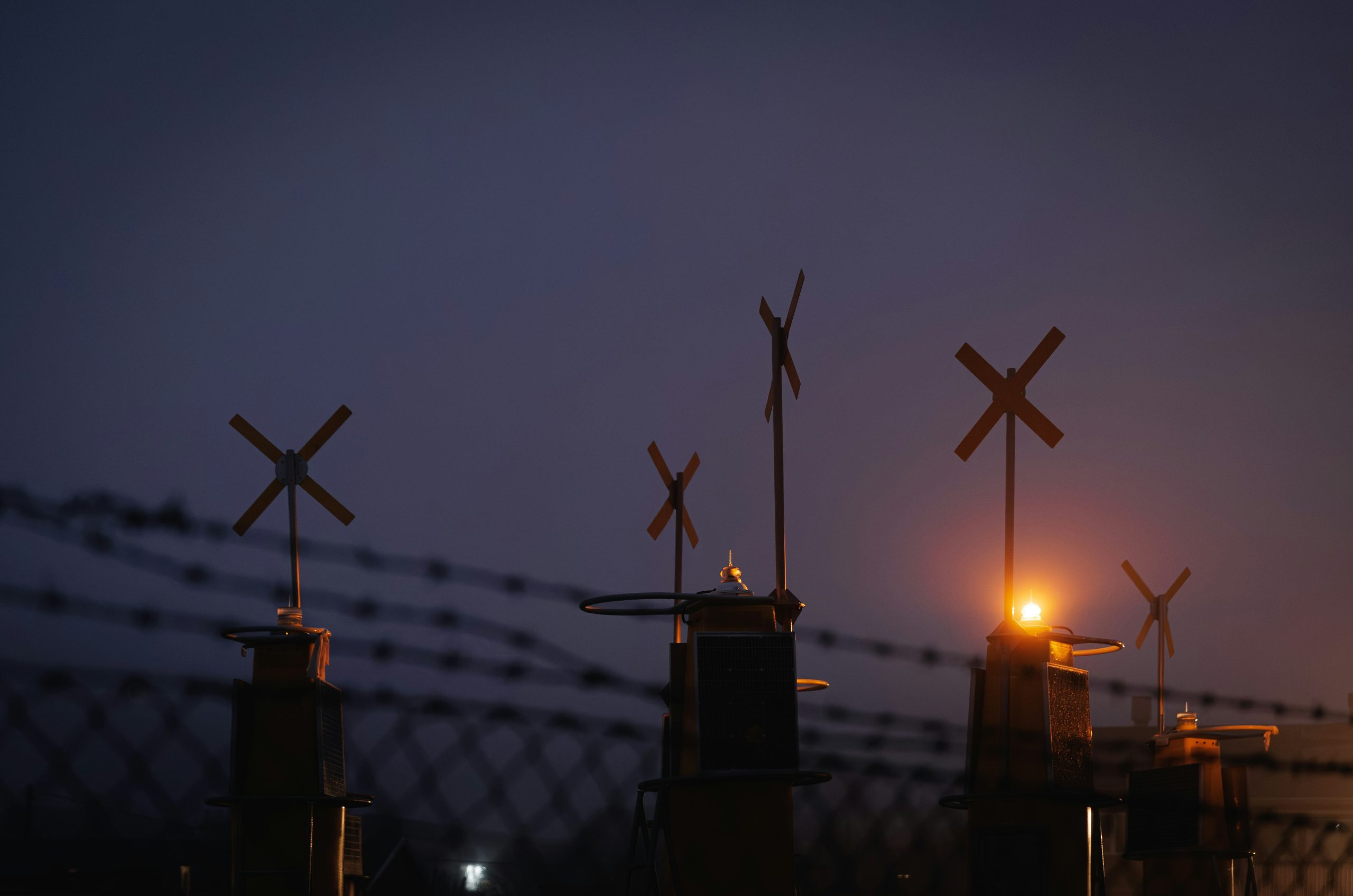 Barbed wire fence with cross-shaped markers at dusk