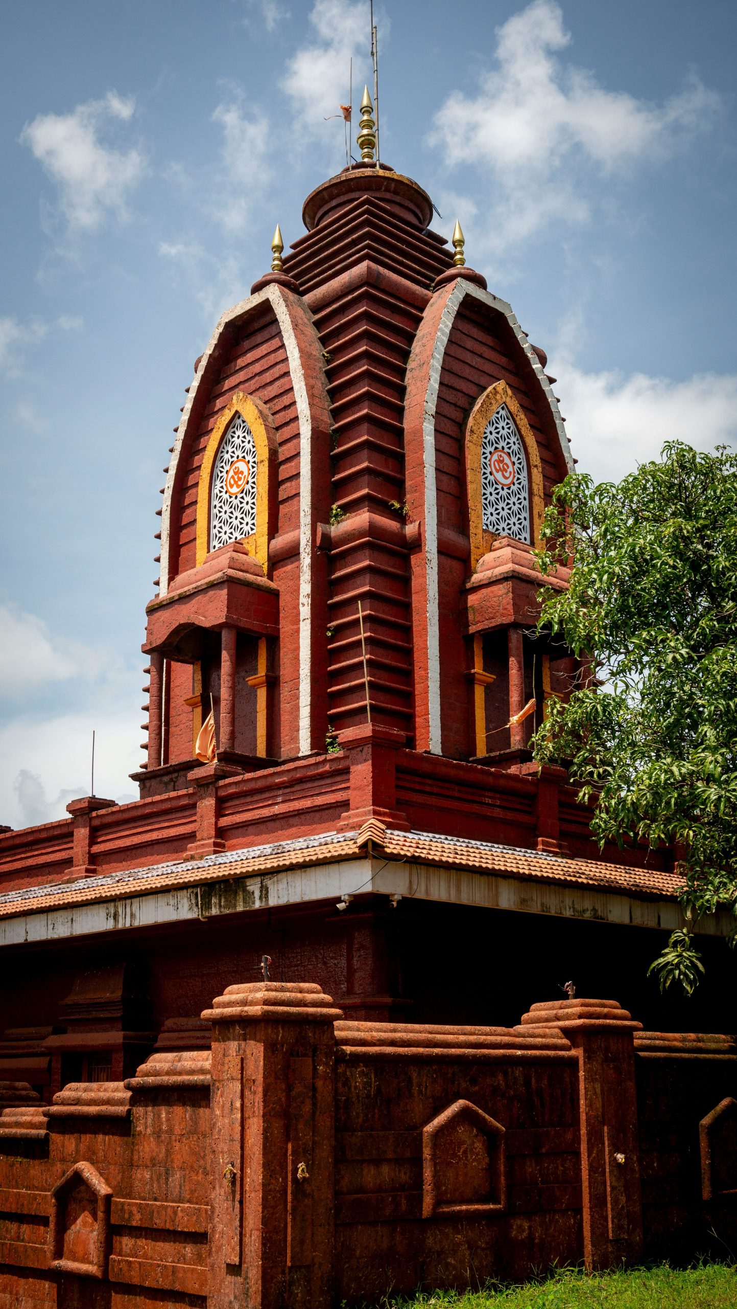 A red temple with ornate windows against a cloudy sky.