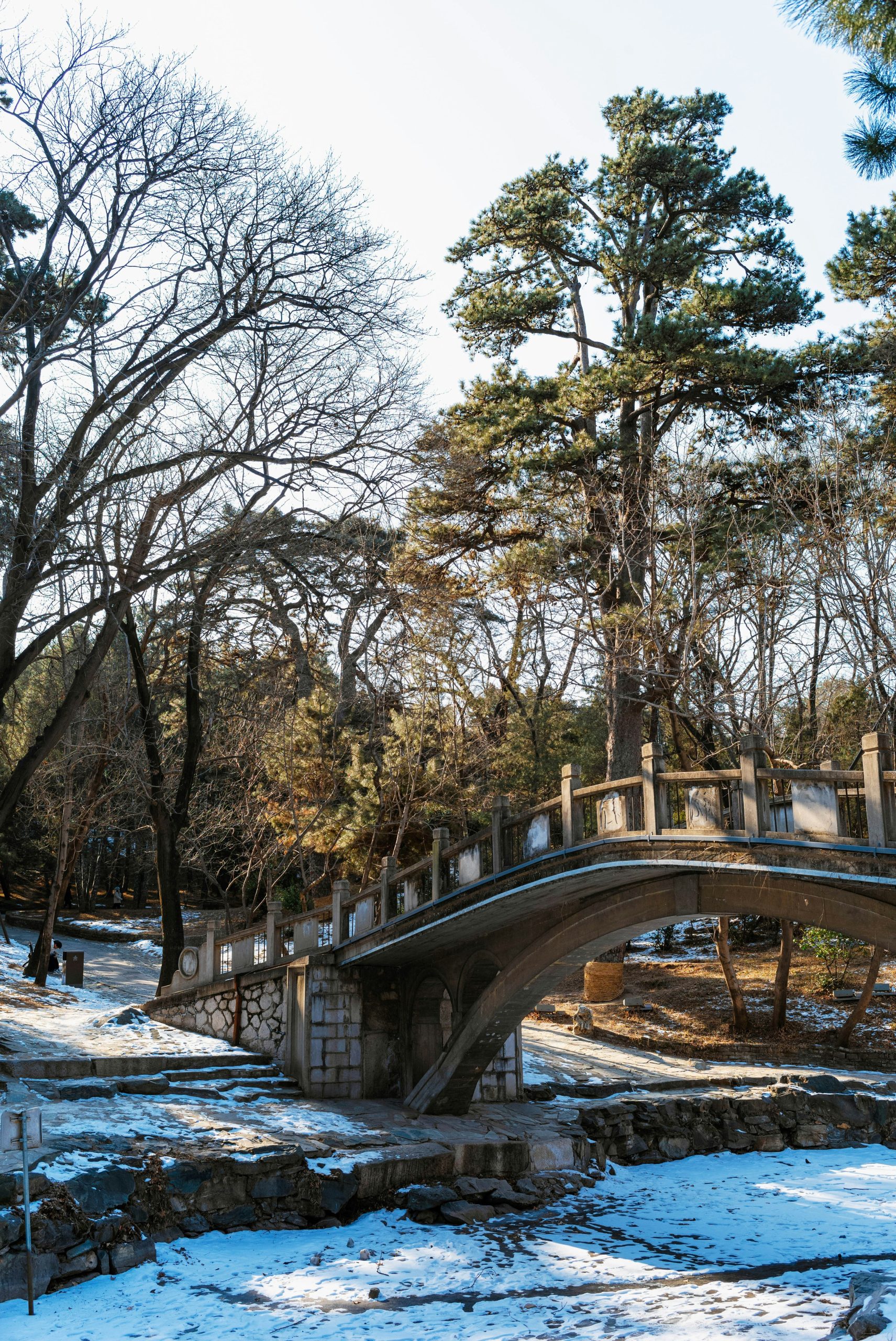 Stone bridge over snowy ground in a park.