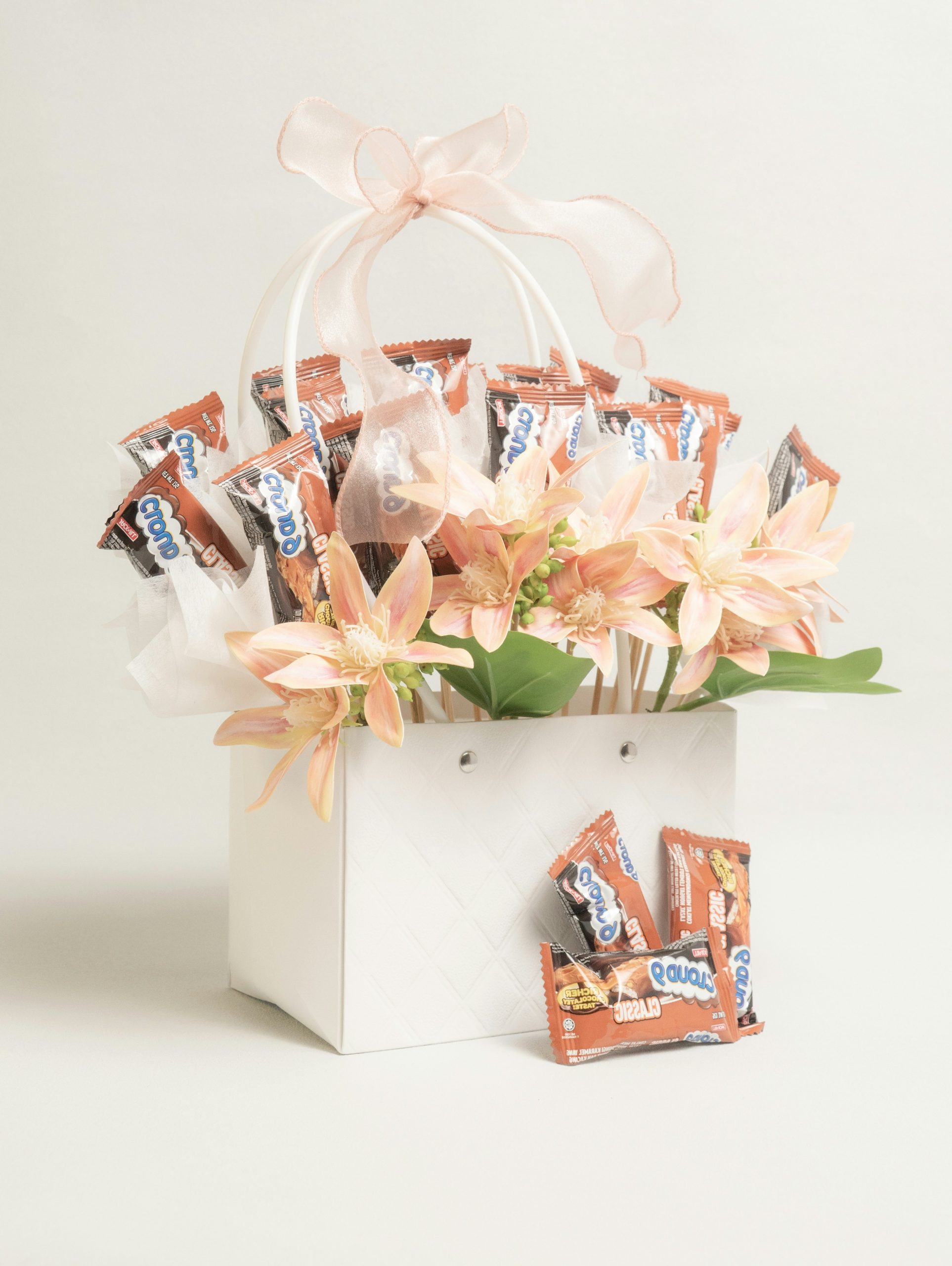 A white gift bag filled with candy bars and flowers.