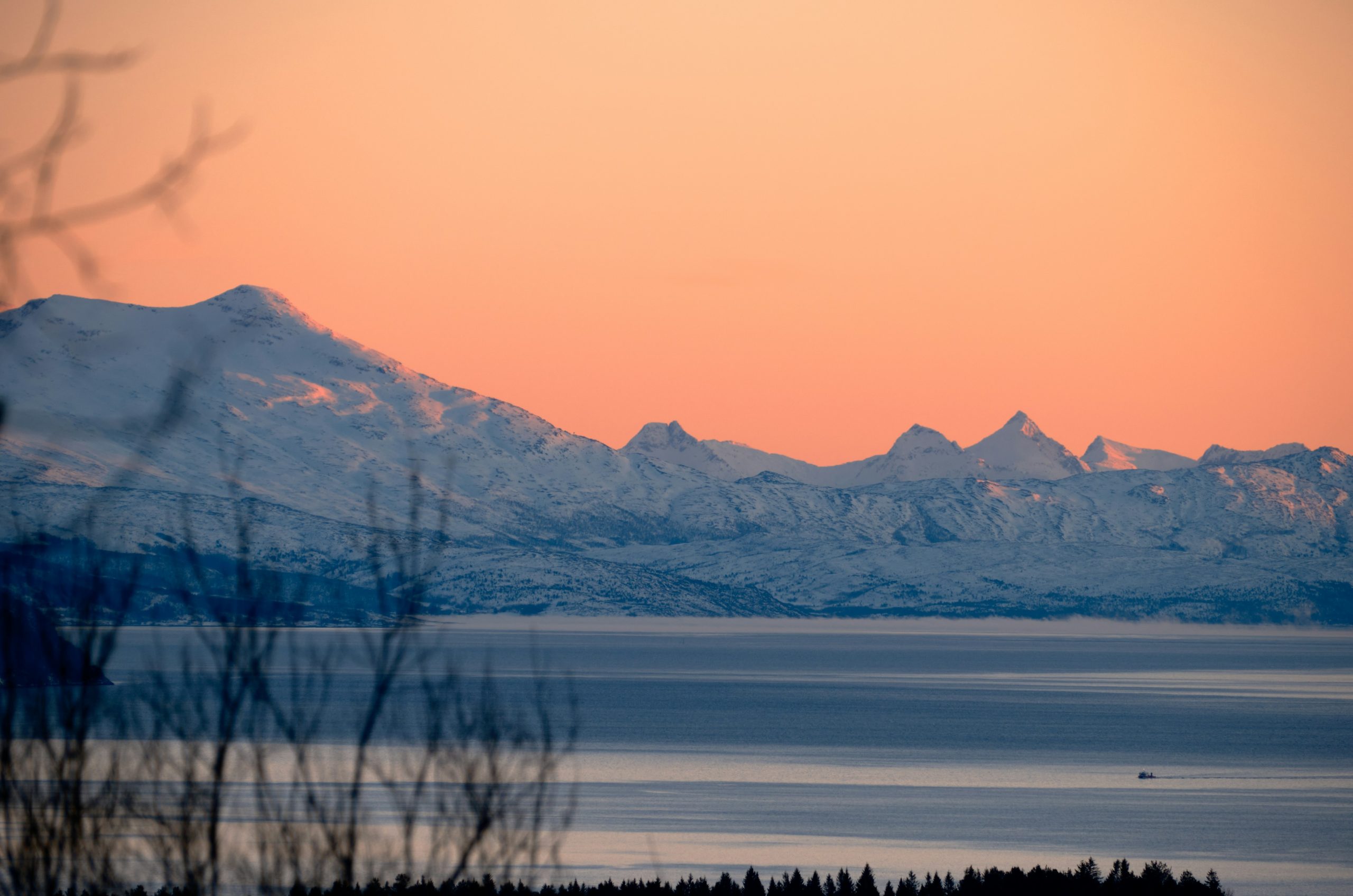 Snow-capped mountains at sunset over a calm sea.