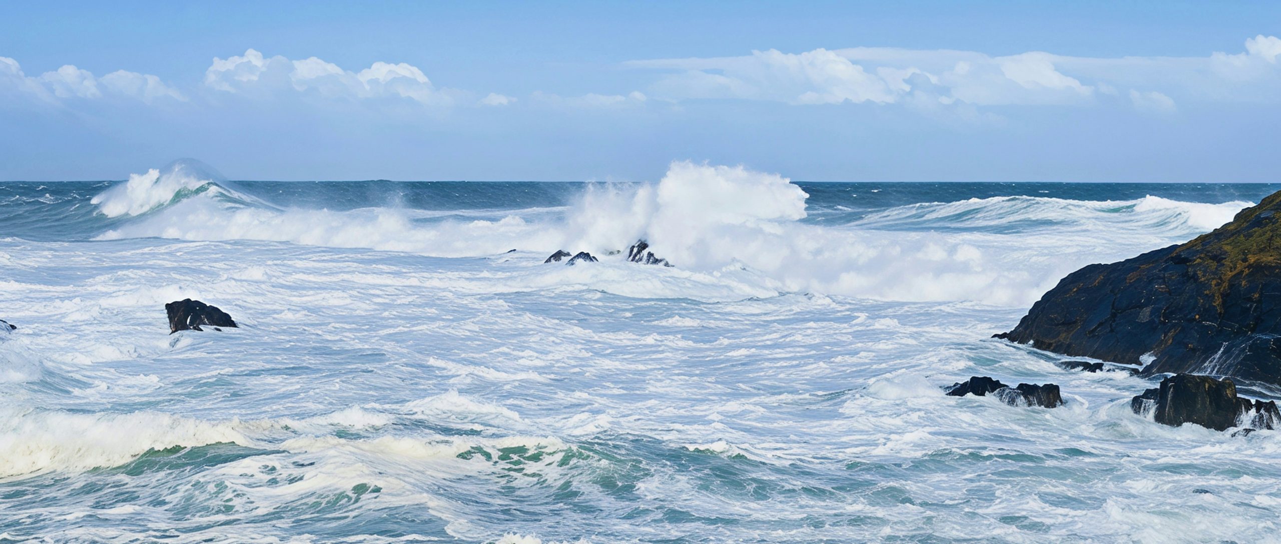 Crashing waves against rocky shore under a blue sky.