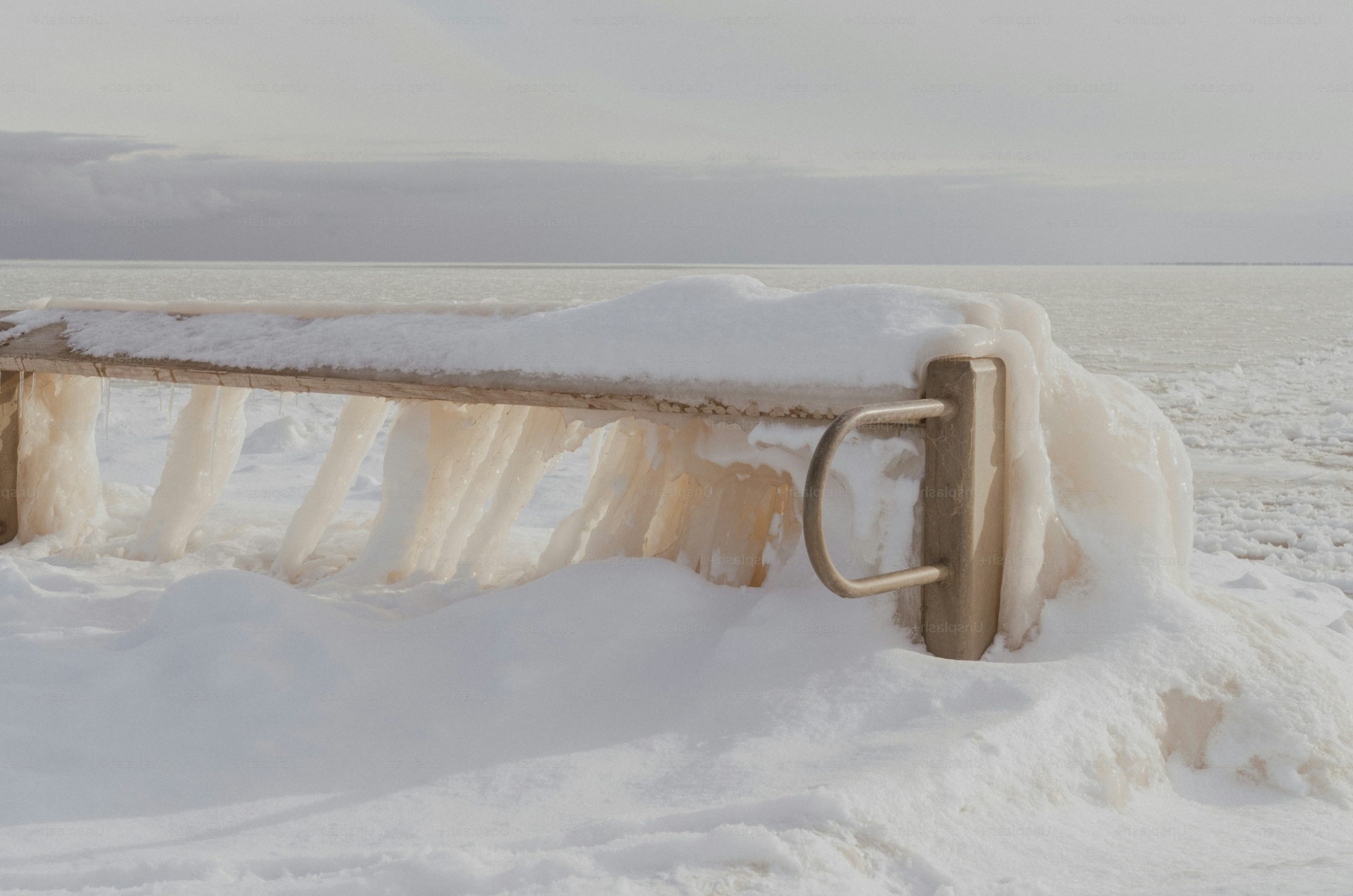 A snow-covered bench with icy details by the sea