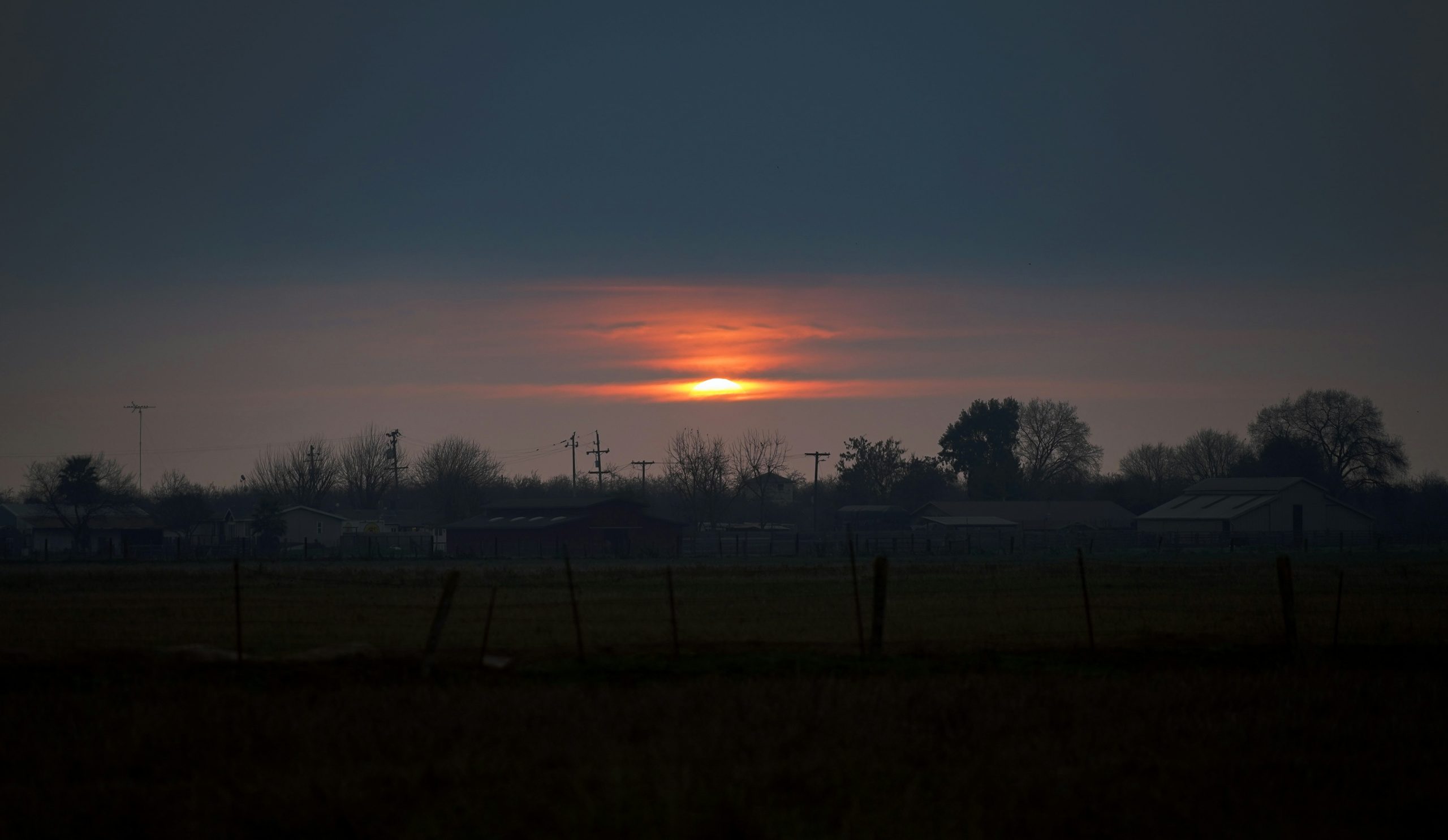 Sunrise over a dark, rural landscape.