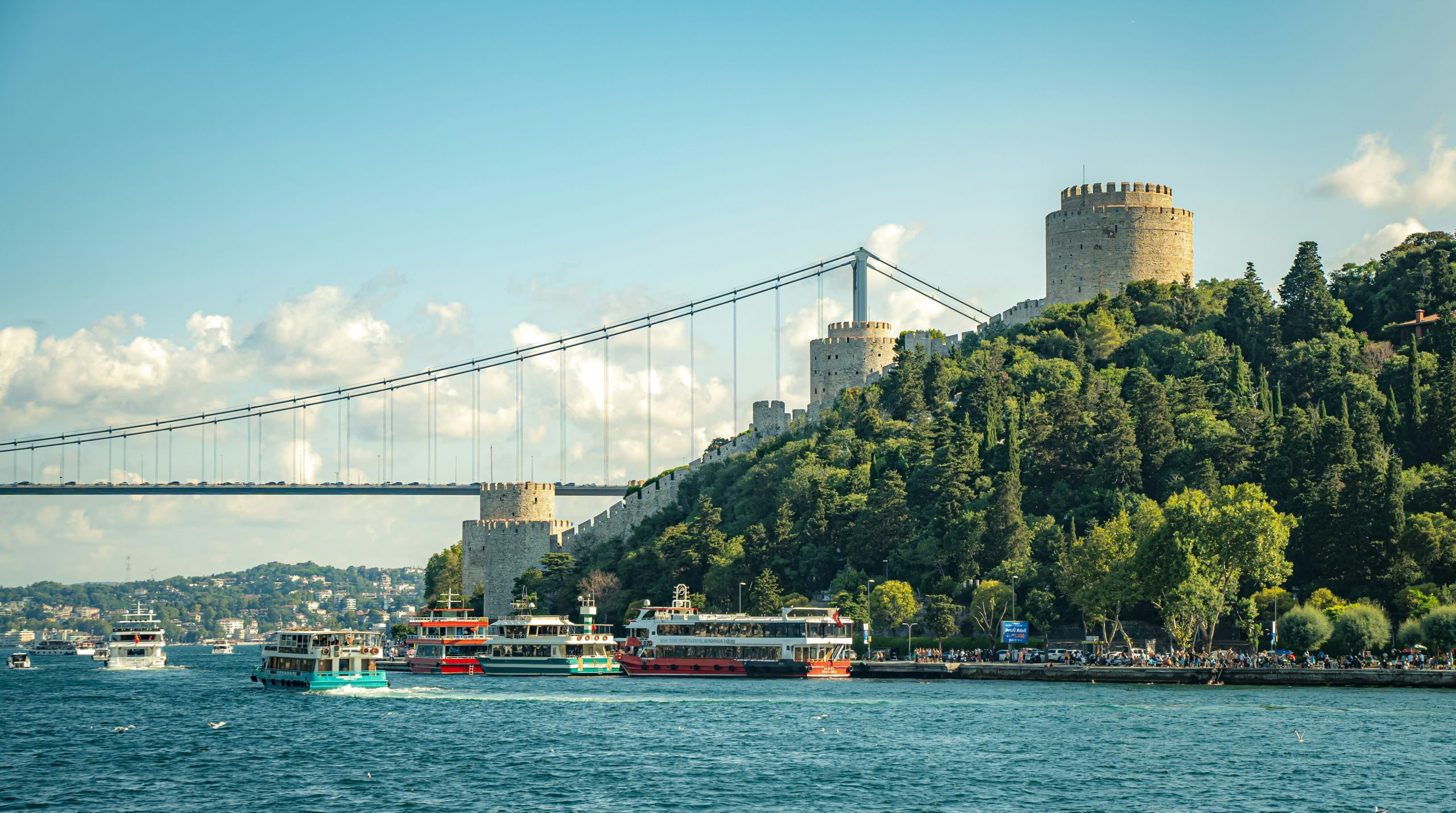 Castle on a hill overlooking a blue river with boats.