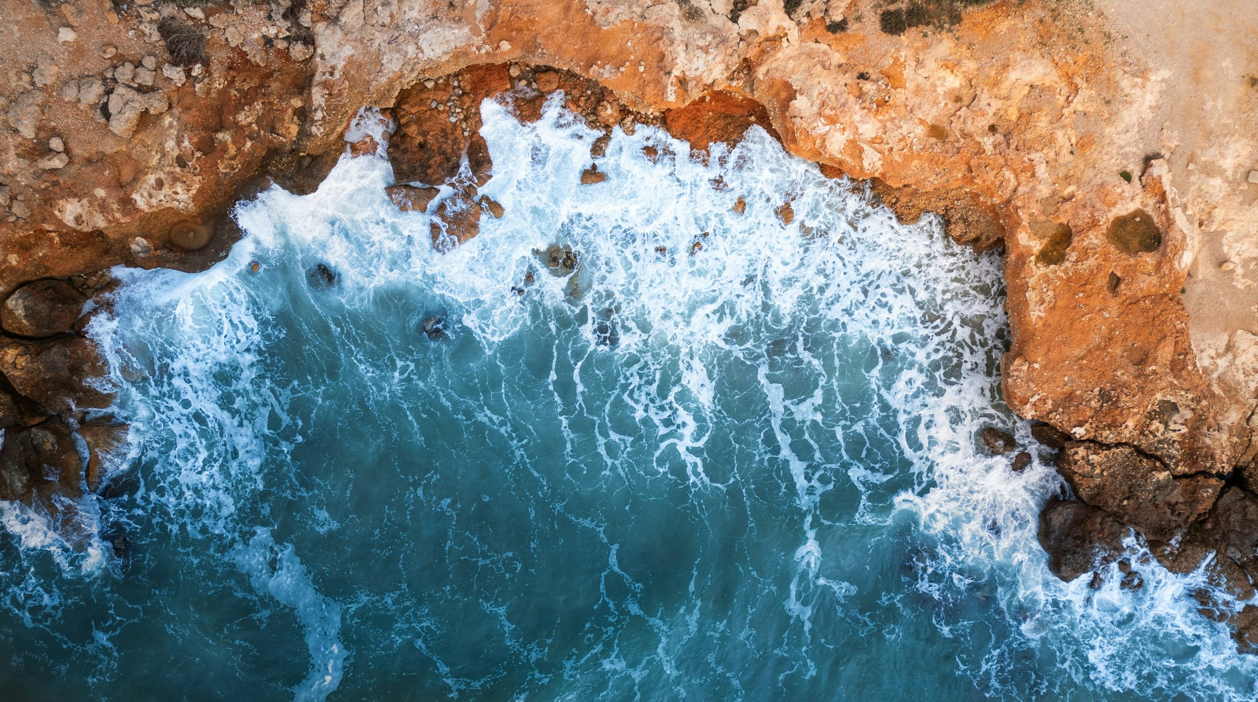 Waves crash against a rocky coastline from above