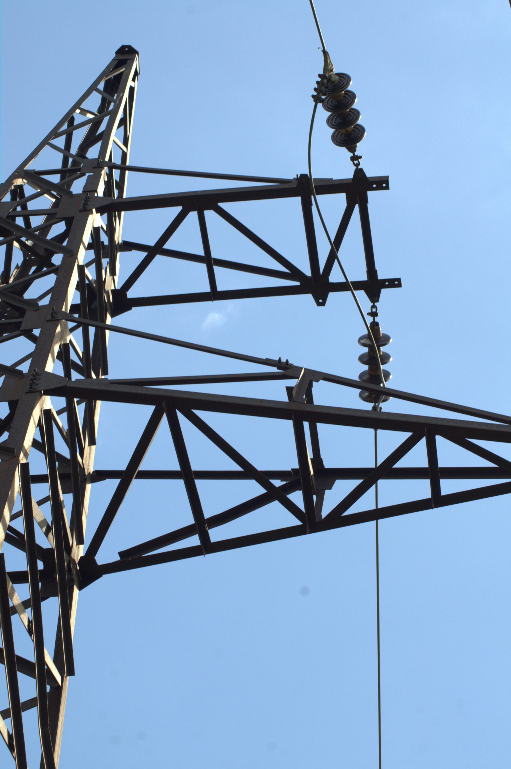 Close-up of a metal power line tower against blue sky