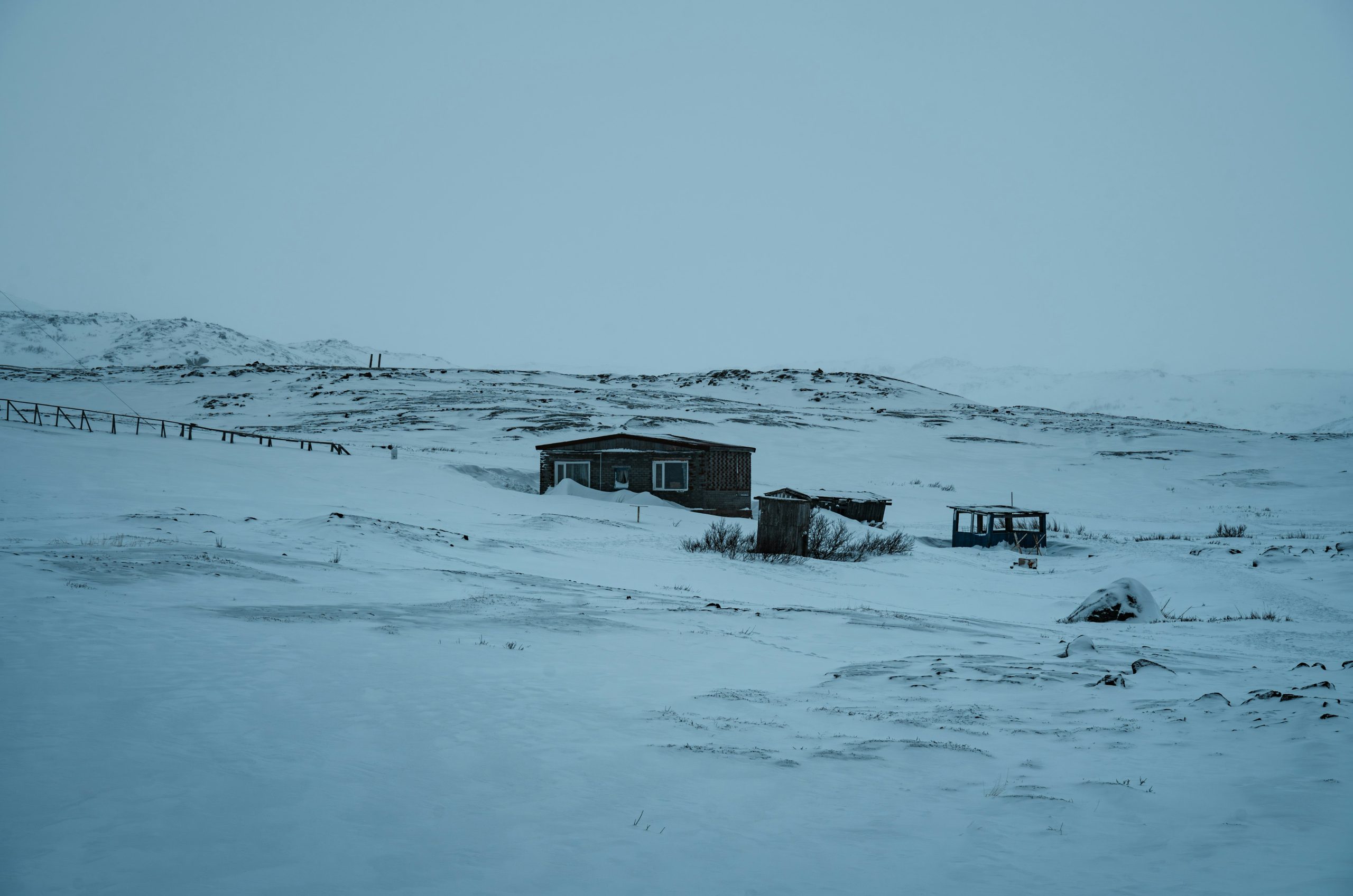 Two small wooden structures in a snowy, desolate landscape.