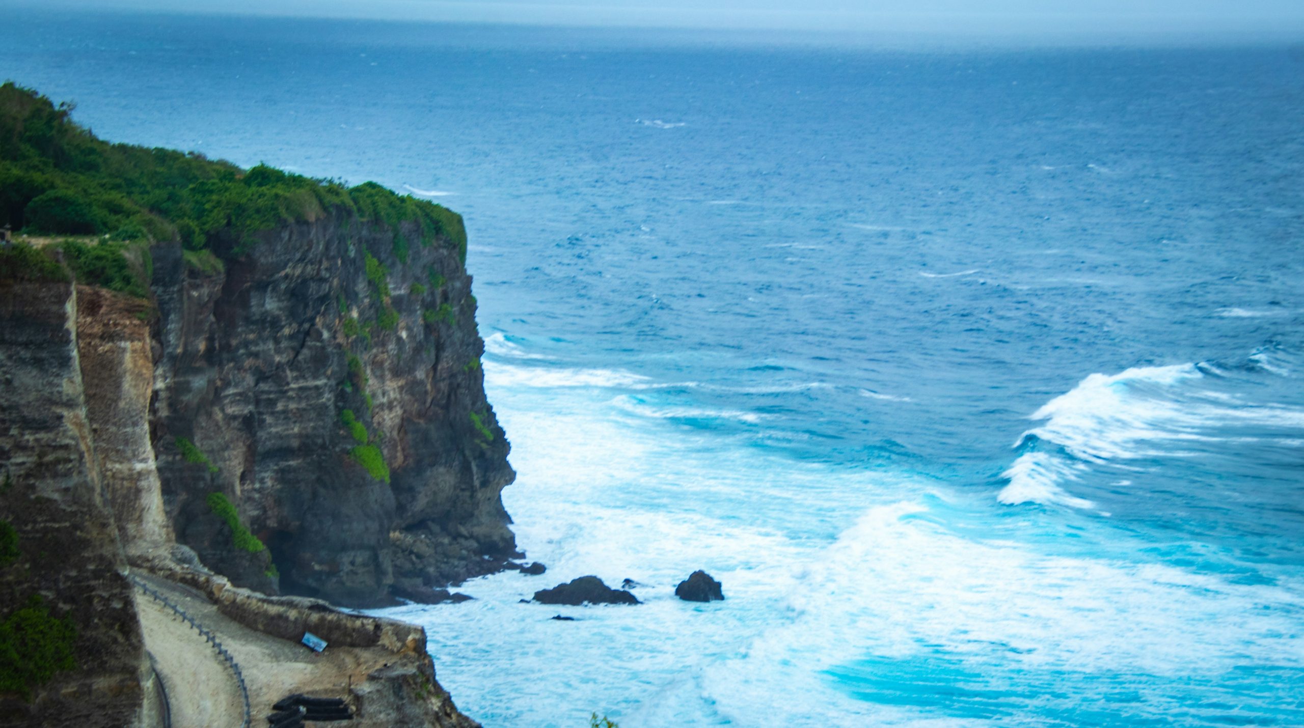 Rugged cliff overlooking a turbulent ocean with crashing waves.