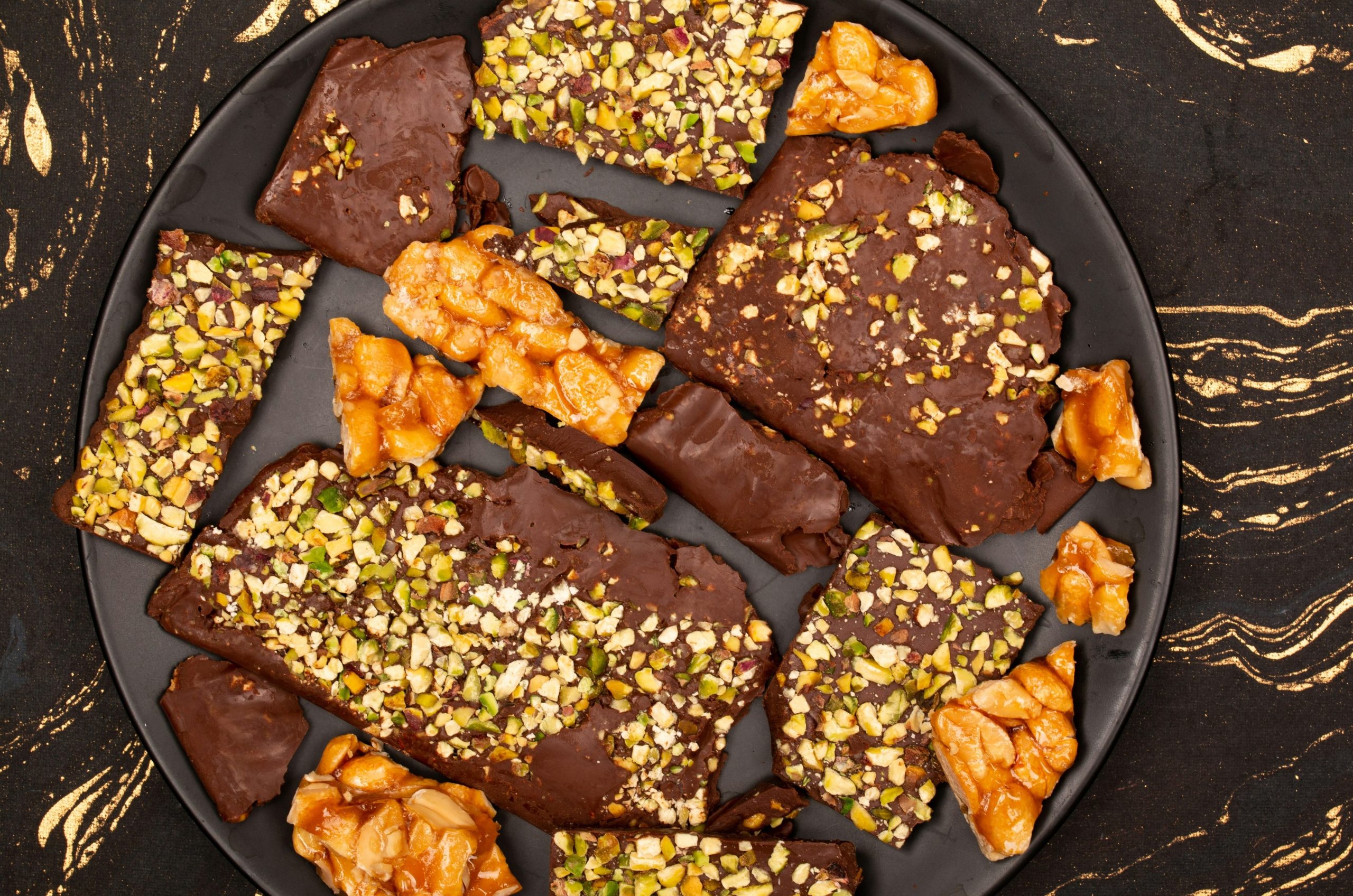 Chocolate bark with nuts and pistachios on a dark plate.