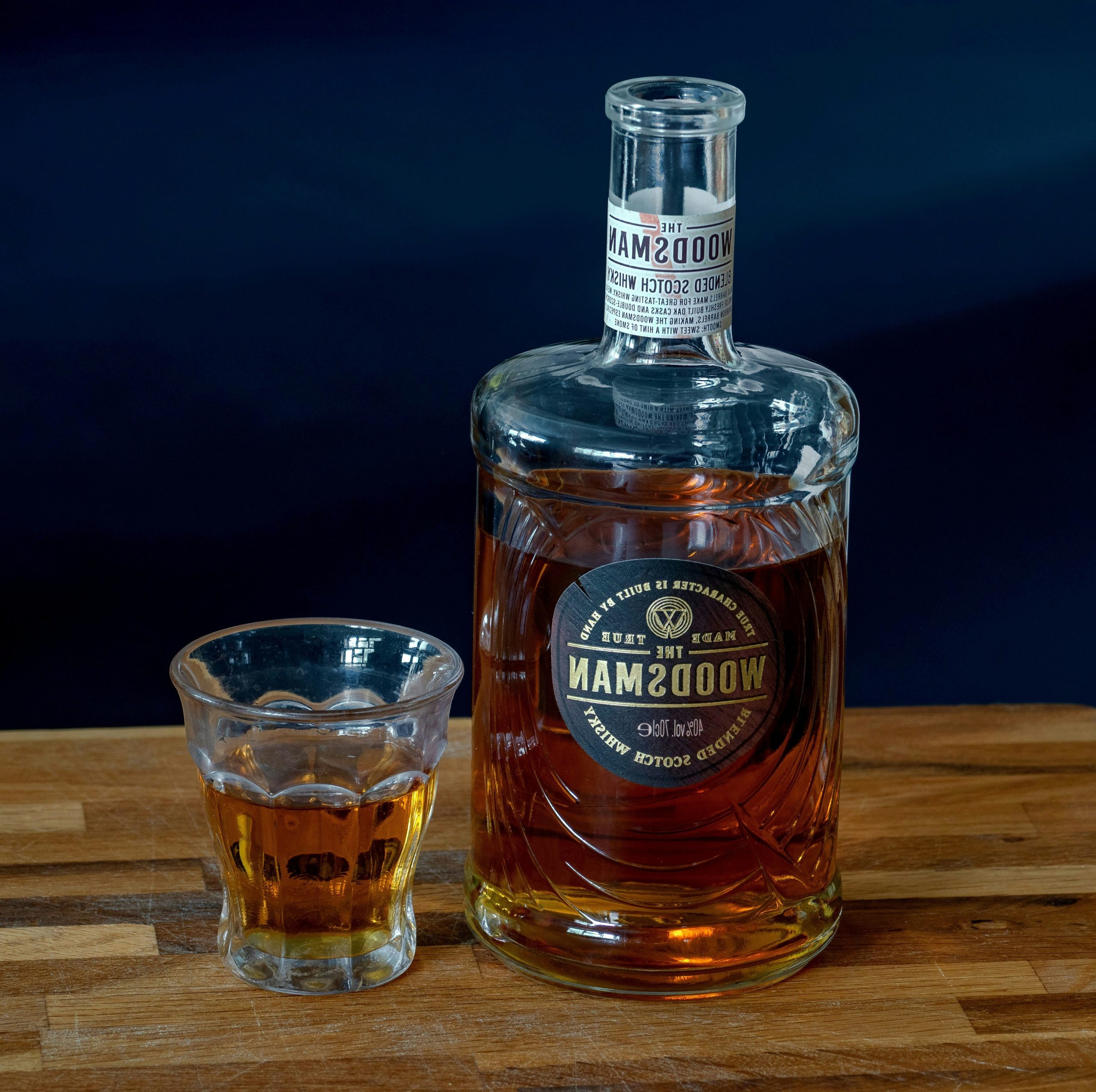 A bottle of woodsman whiskey with a shot glass